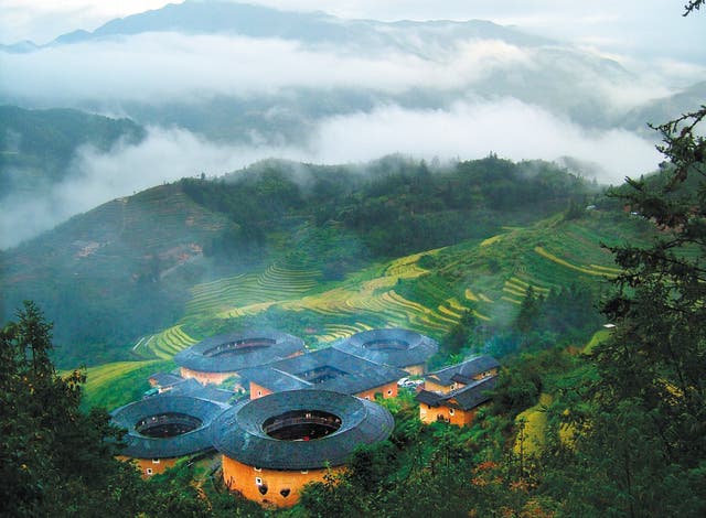 <p>A bird’s eye view of the earthen buildings in Nanjing county, Fujian province, surrounded by forests and tiered farmlands</p>