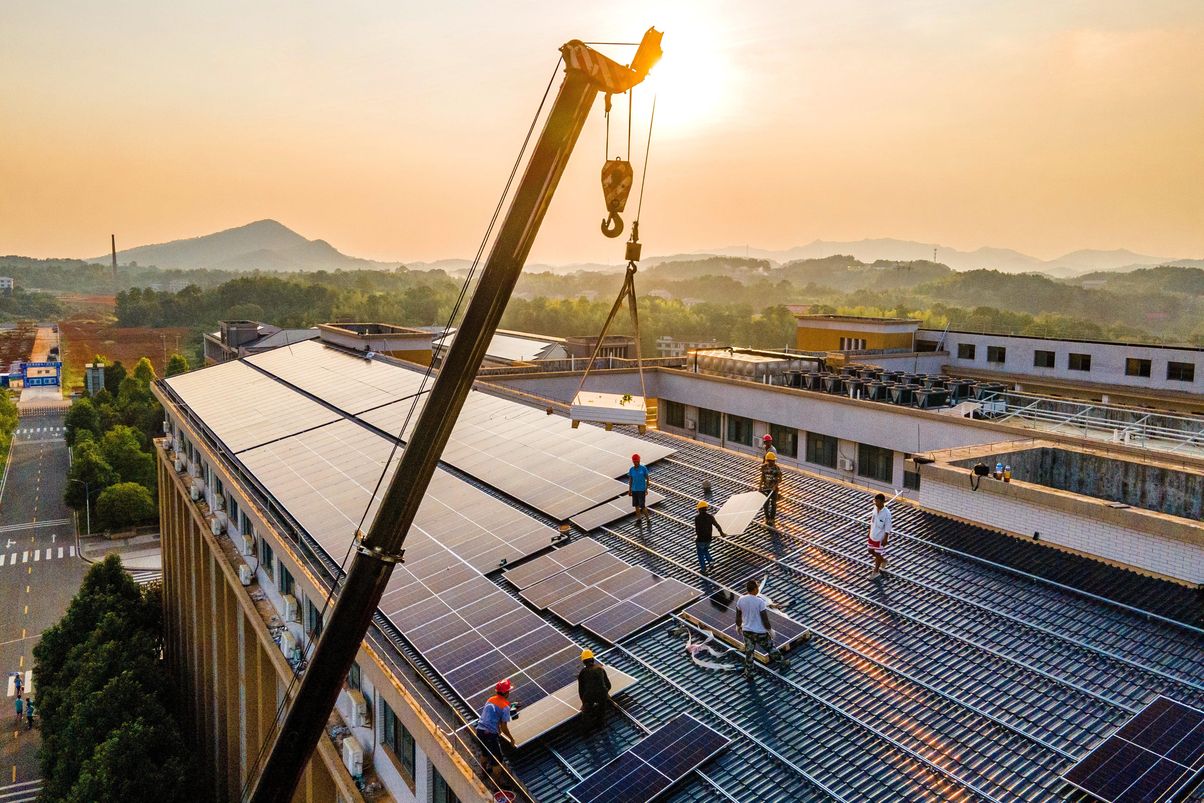 A crane is used to lift solar panels onto the roof of a building at the No 1 Middle School in Shuangfeng county, Hunan province, on 18 August, 2023