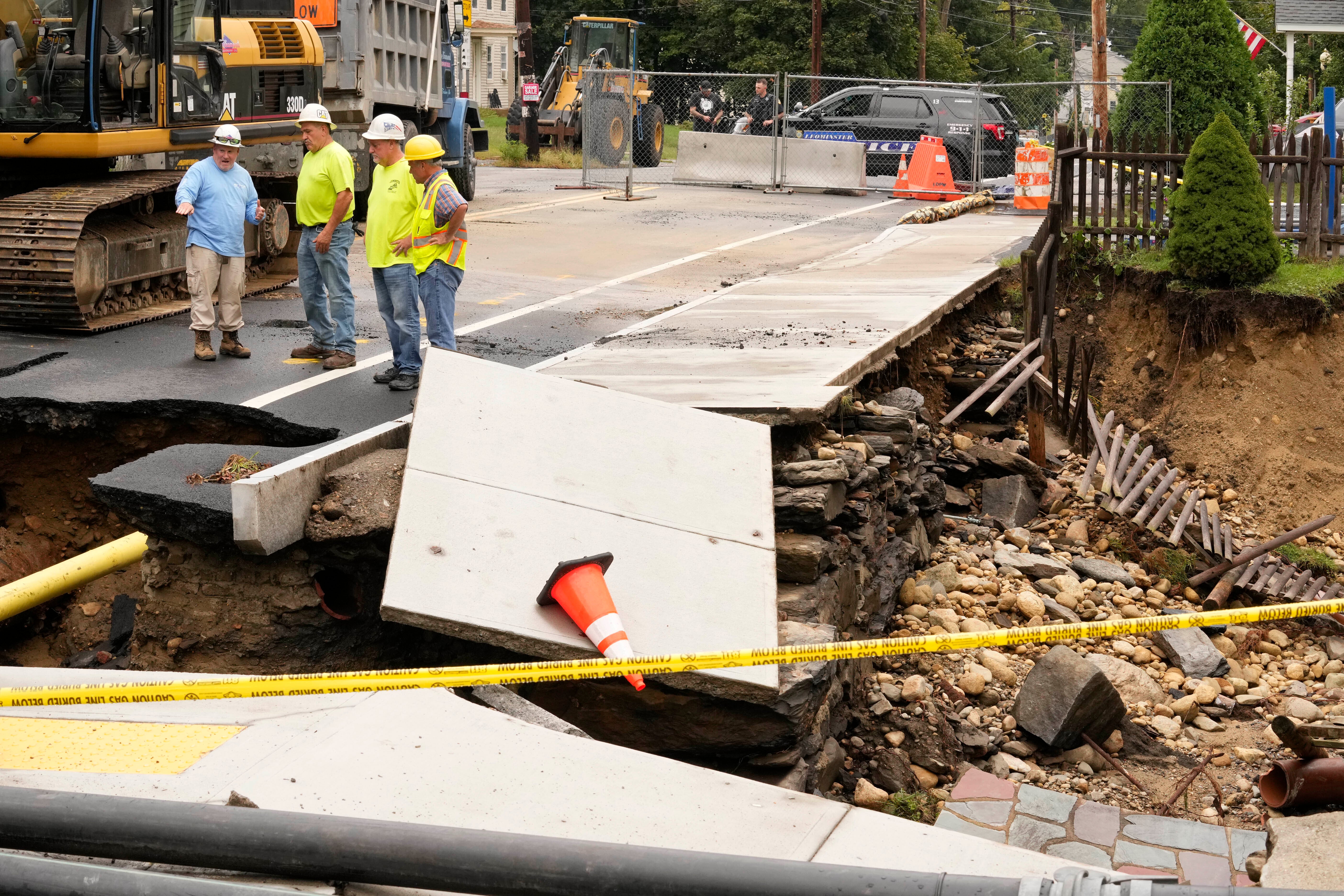 Public works officials examine the damage to a road and front yard that was washed away by recent flooding, Wednesday, Sept. 13, 2023, in Leominster, Mass.