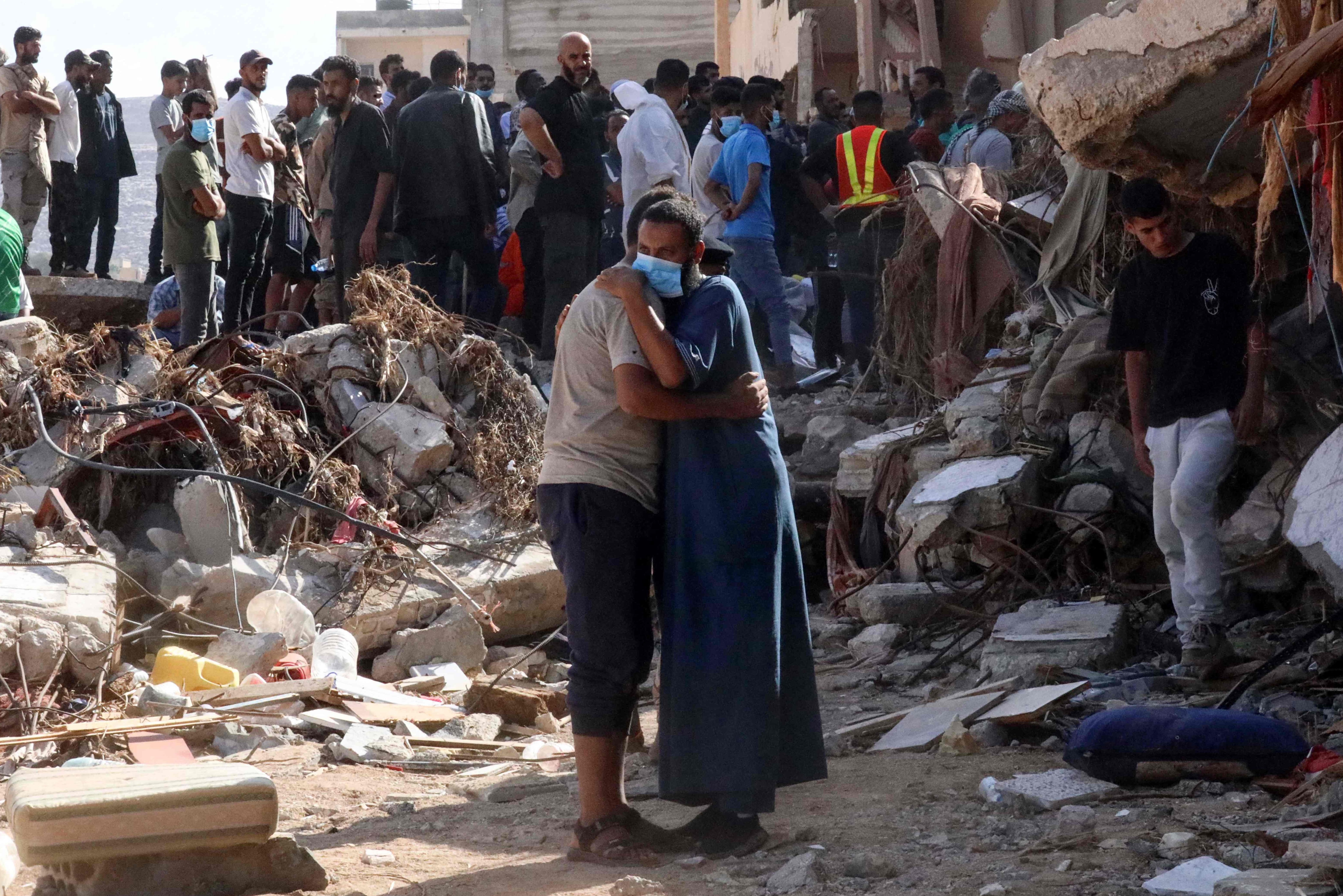 <p>Two men comfort each other in the devastated Libyan city of Derna</p>