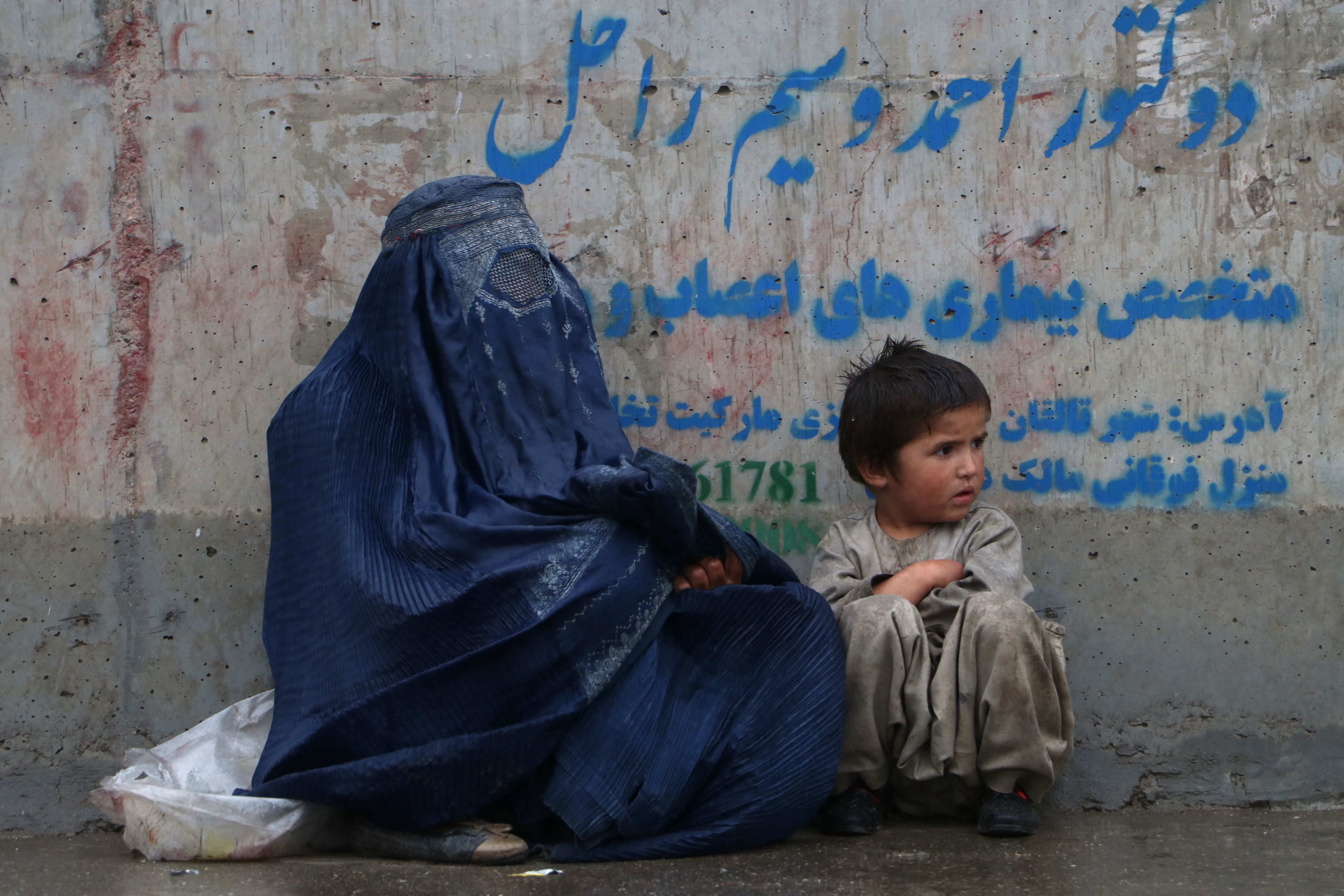 An Afghan woman and a child sits along a path, after a drizzle in Fayzabad district of Badakhshan province