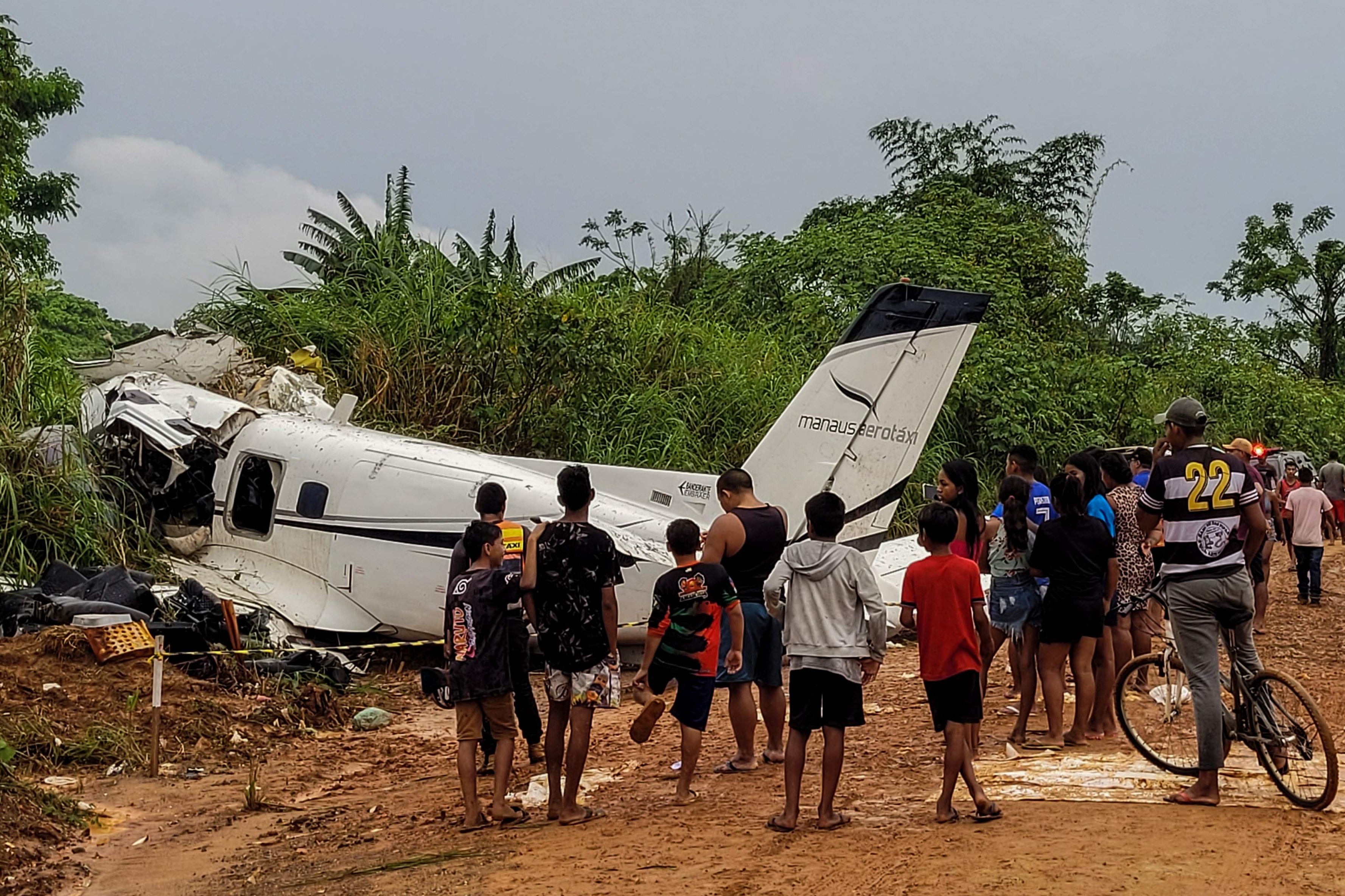 People stand looking at the site where an Embraer EMB-110 aircraft of the Manaus Aerotaxi airline crashed, causing the deaths of 14 people during the plane's landing the previous day at Barcelos airport