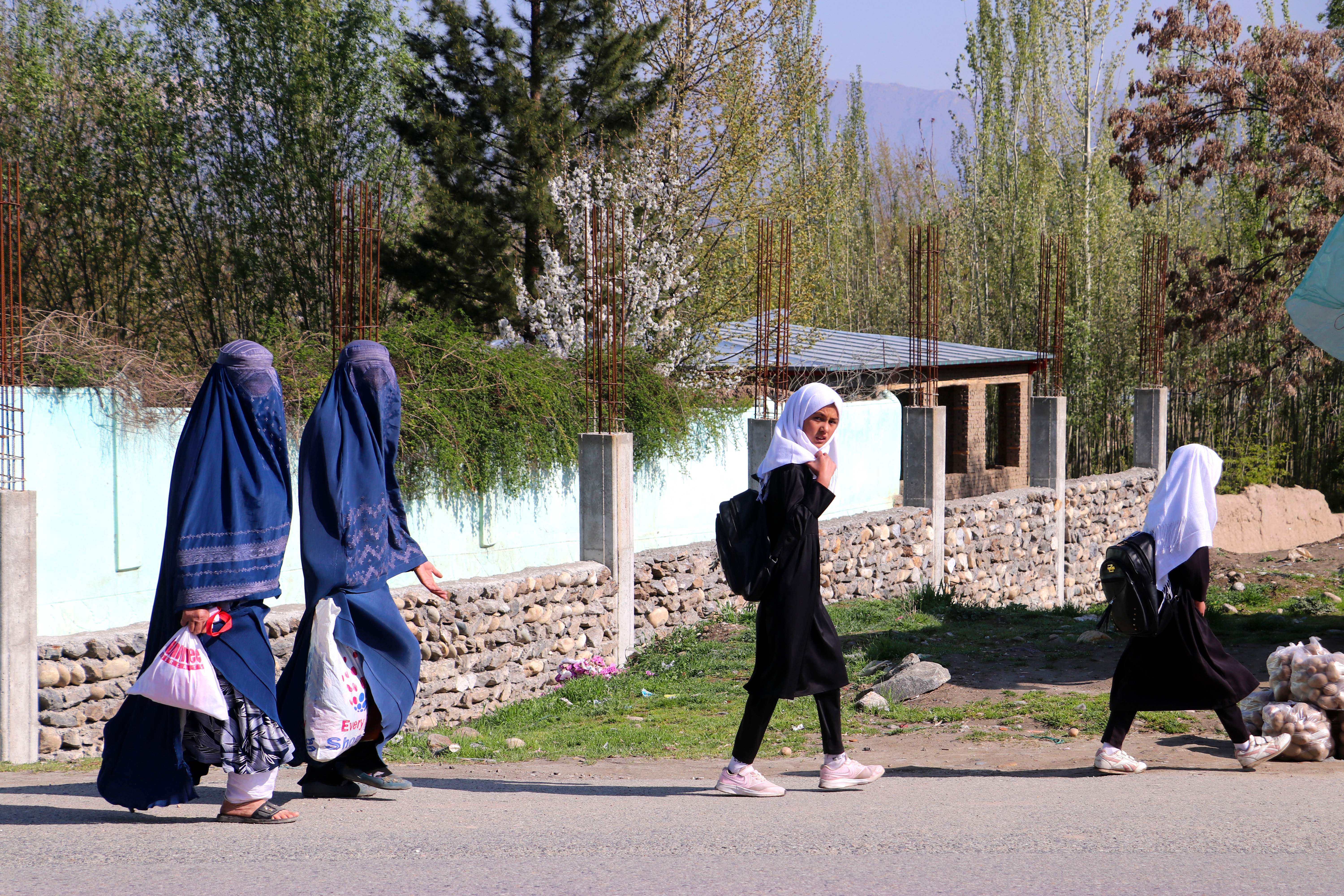 Afghan burqa-clad women along with school girls walk along a road in Fayzabad district of Badakhshan province