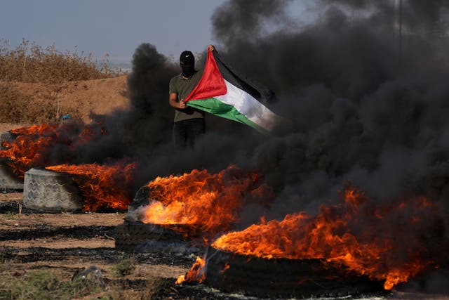 <p>A masked Palestinian protester waves his national flag next to burning tires during clashes with Israeli security forces along the frontier with Israel</p>