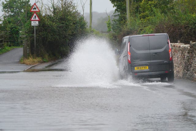 <p>A van is driven through floodwater on a road in to Dawlish, Devon</p>