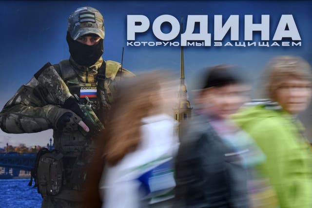 <p>Pedestrians walk past a public placard depicting the portrait of a Russian serviceman and reading "The Motherland we defend" during a public military-themed exhibition in Saint Petersburg</p>