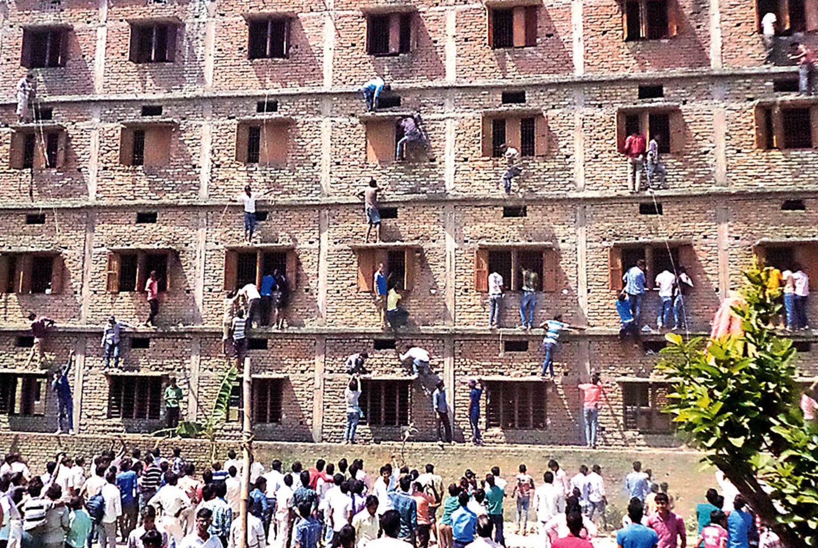 In this photograph taken on 19 March 2015, Indian relatives of students taking school exams climb the walls of the exam building to help pass candidates answers to questions in Vaishali in Bihar