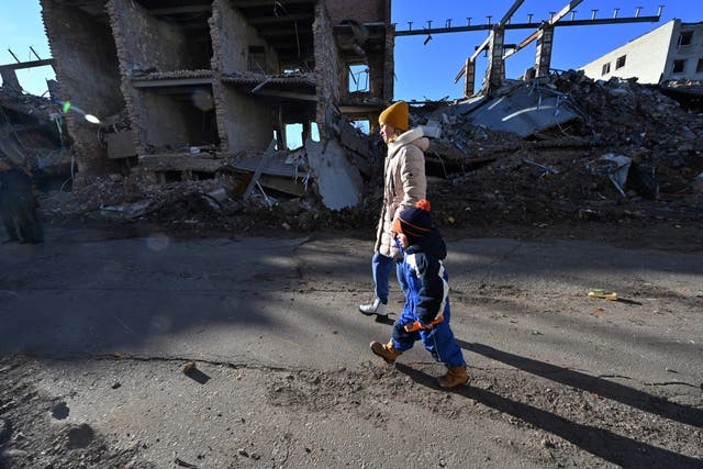 <p>A local resident hold the hand of a child as they walk past a destroyed building following a C-300 missile strike on the Ukrainian city of Kharkiv on 31 March 2023</p>