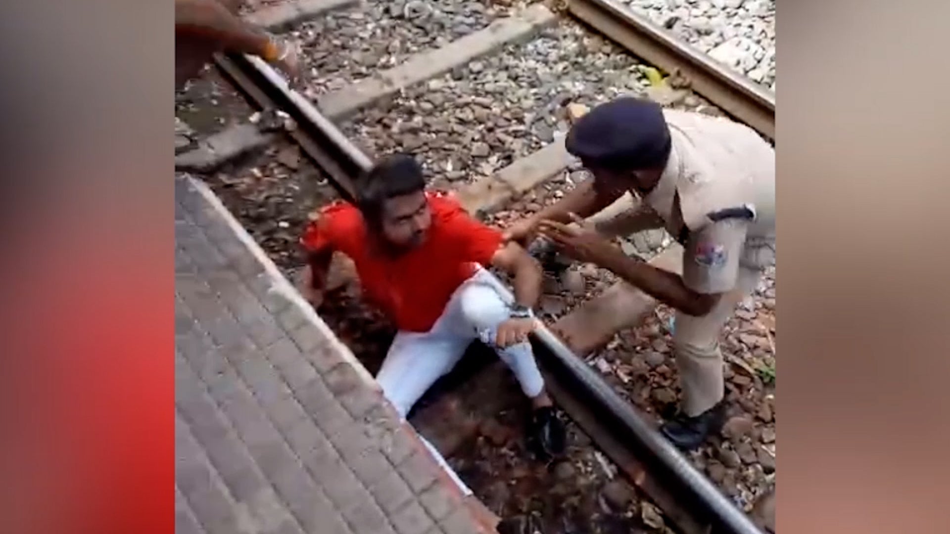 The man is helped up after surviving falling under a moving train in India