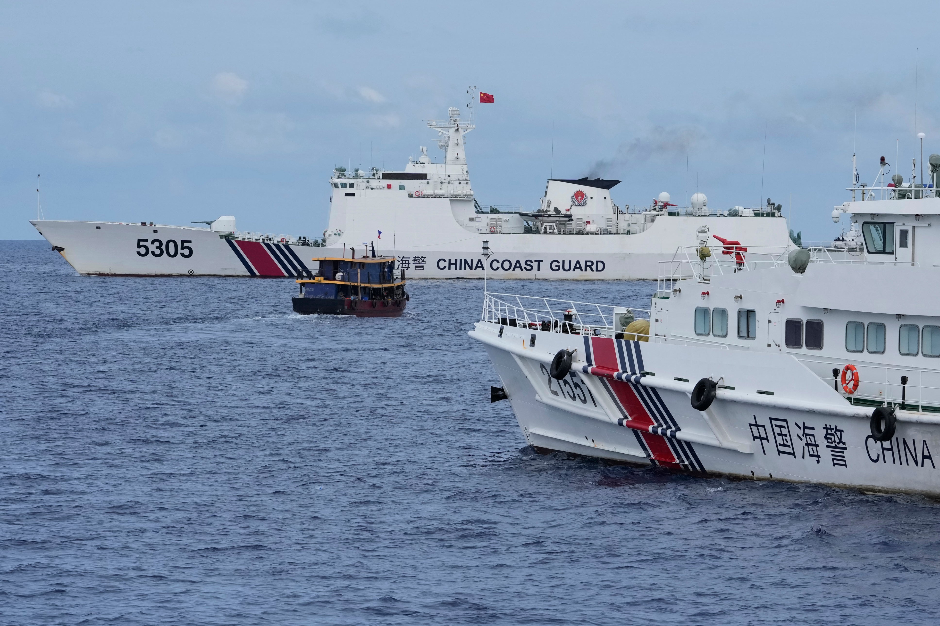 File: A Philippine supply boat, center, maneuvers around Chinese coast guard ships as they try to block its way near Second Thomas Shoal