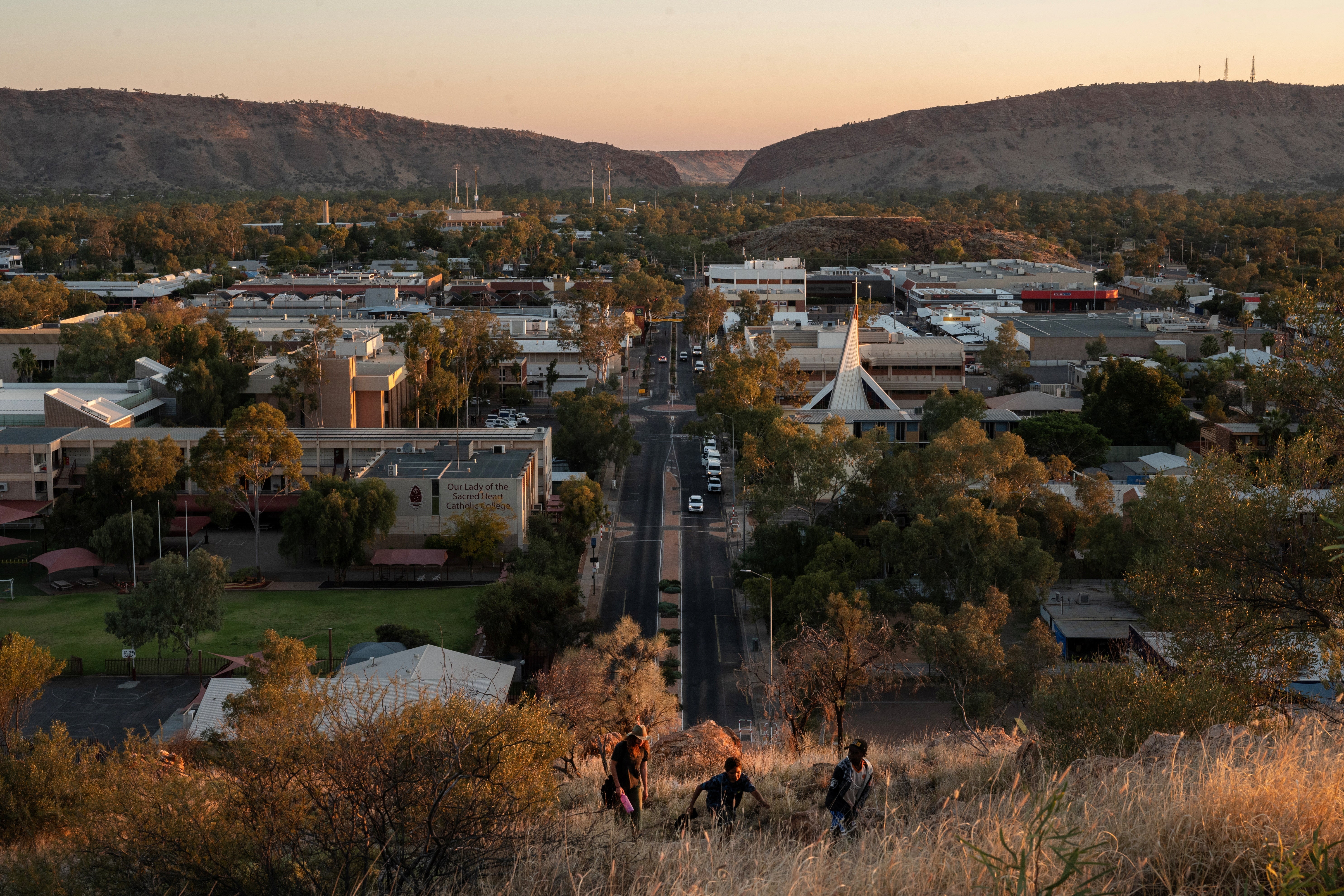 Local residents walk up a hill overlooking Alice Springs at sunset