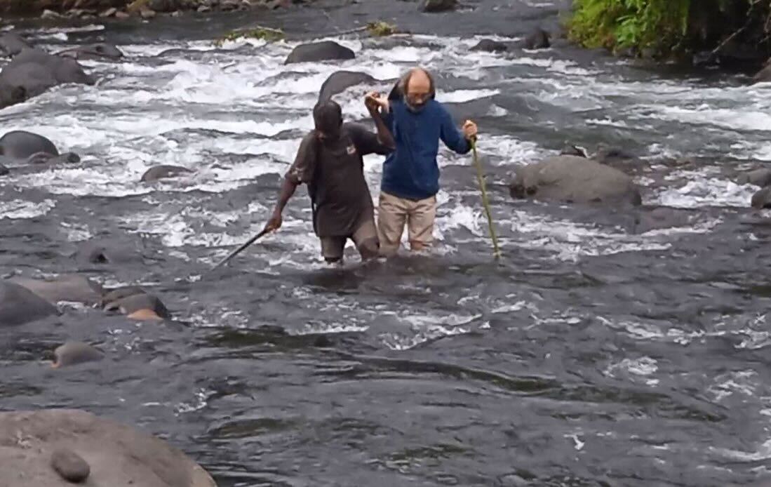 Dr Gianluca Grimalda crossing a stream with a local resident to reach a village in Papua New Guinea