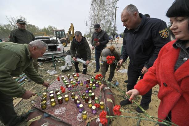 People lay flowers and light candles as Ukrainian rescuers work to remove debris following a Russian strike