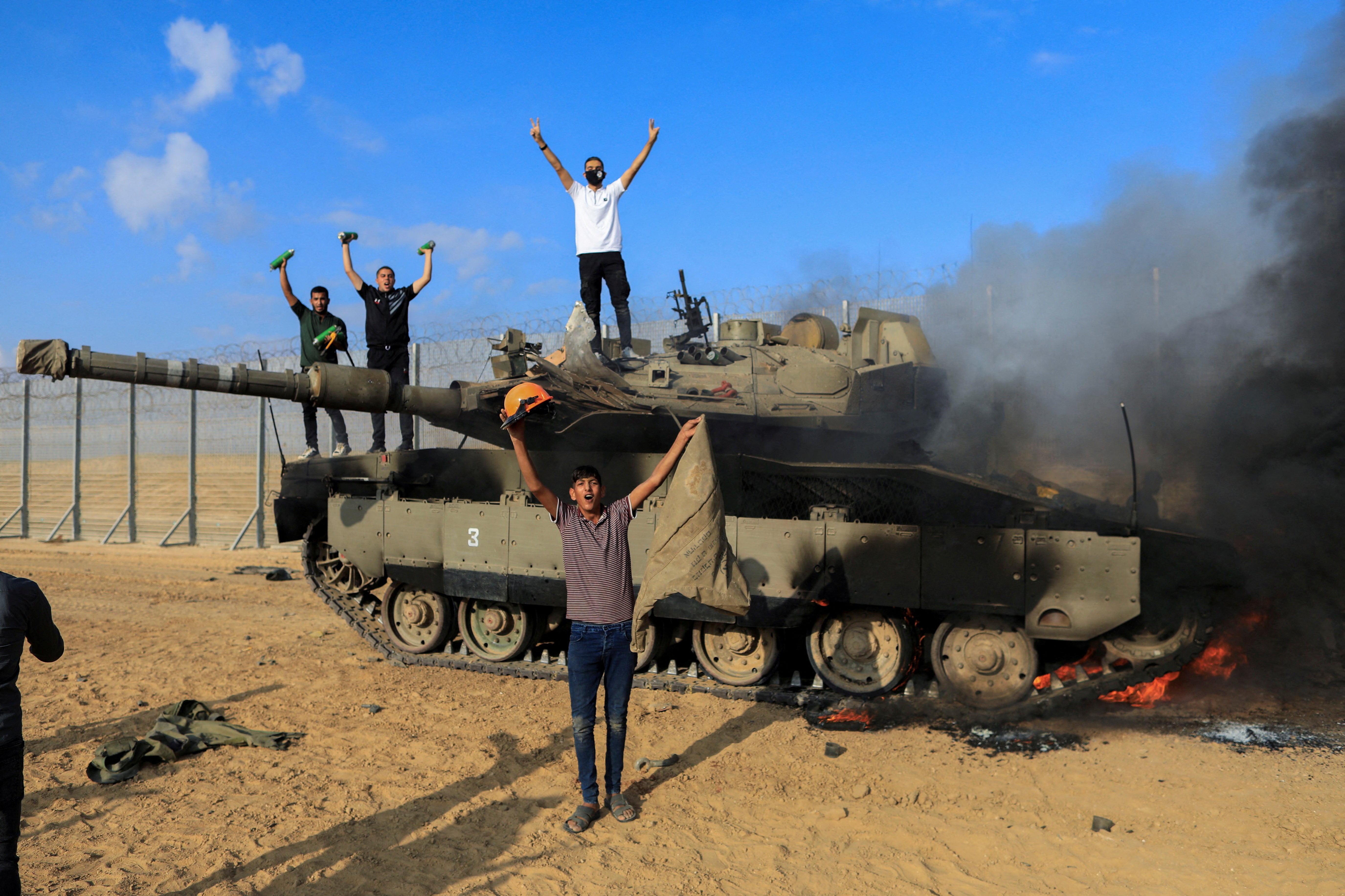 Palestinians celebrate as an Israeli military vehicle burns after it was hit by Palestinian gunmen
