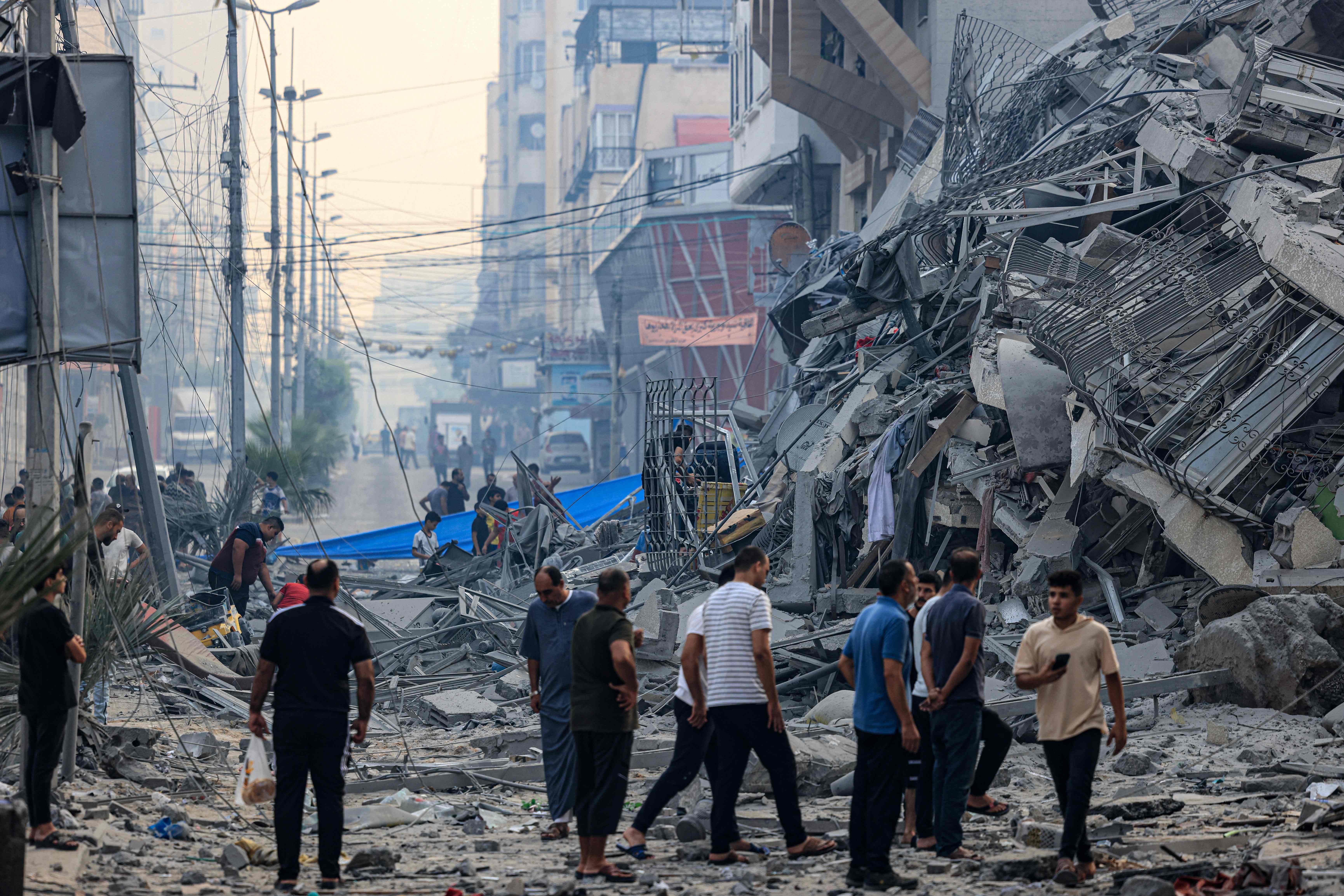 Residents walk along a debris-strewn street in front of a building that collapse during an Israeli air strike