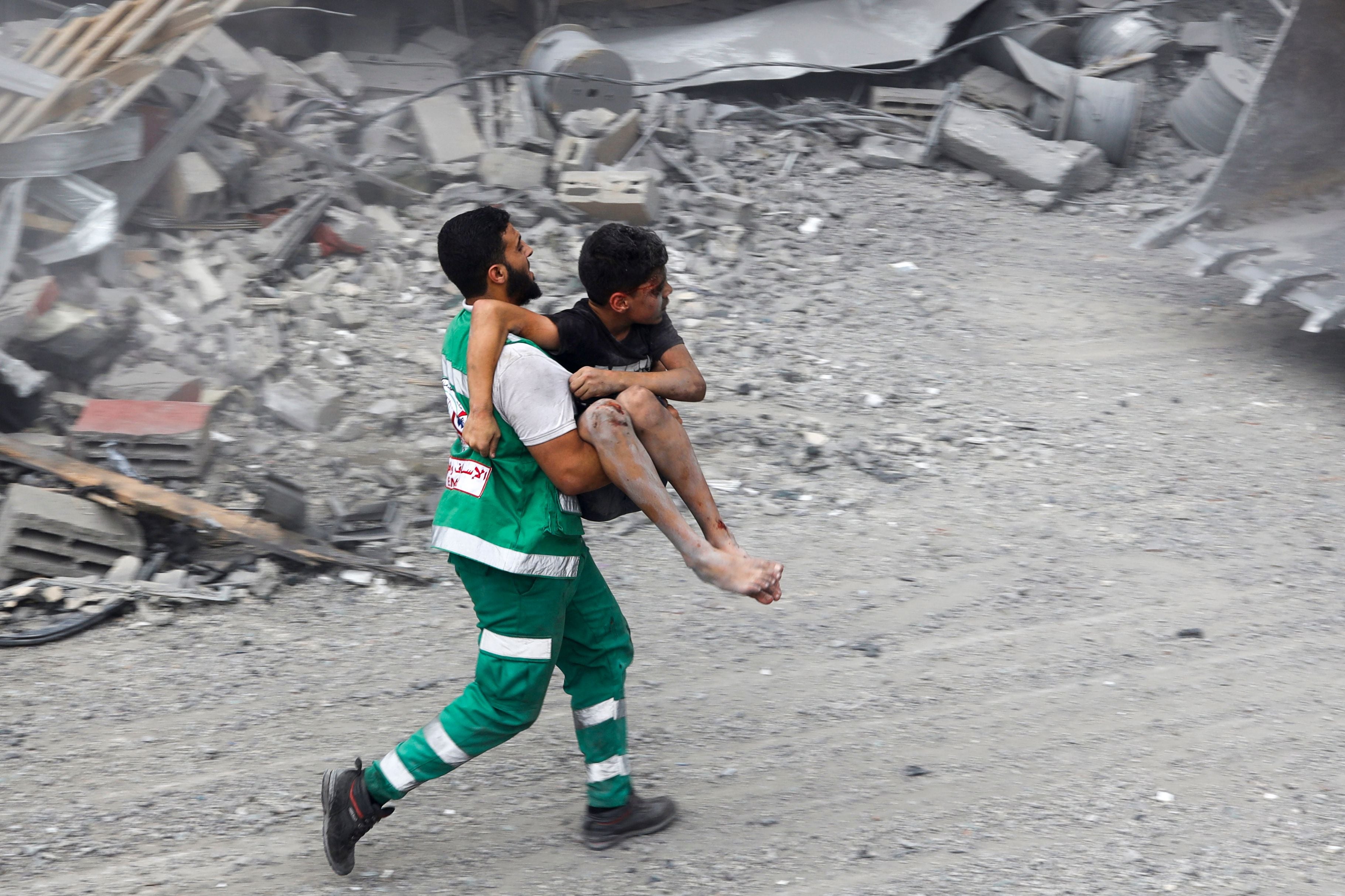 A member of the Palestinian civil defence carries a wounded boy rescued from rubble