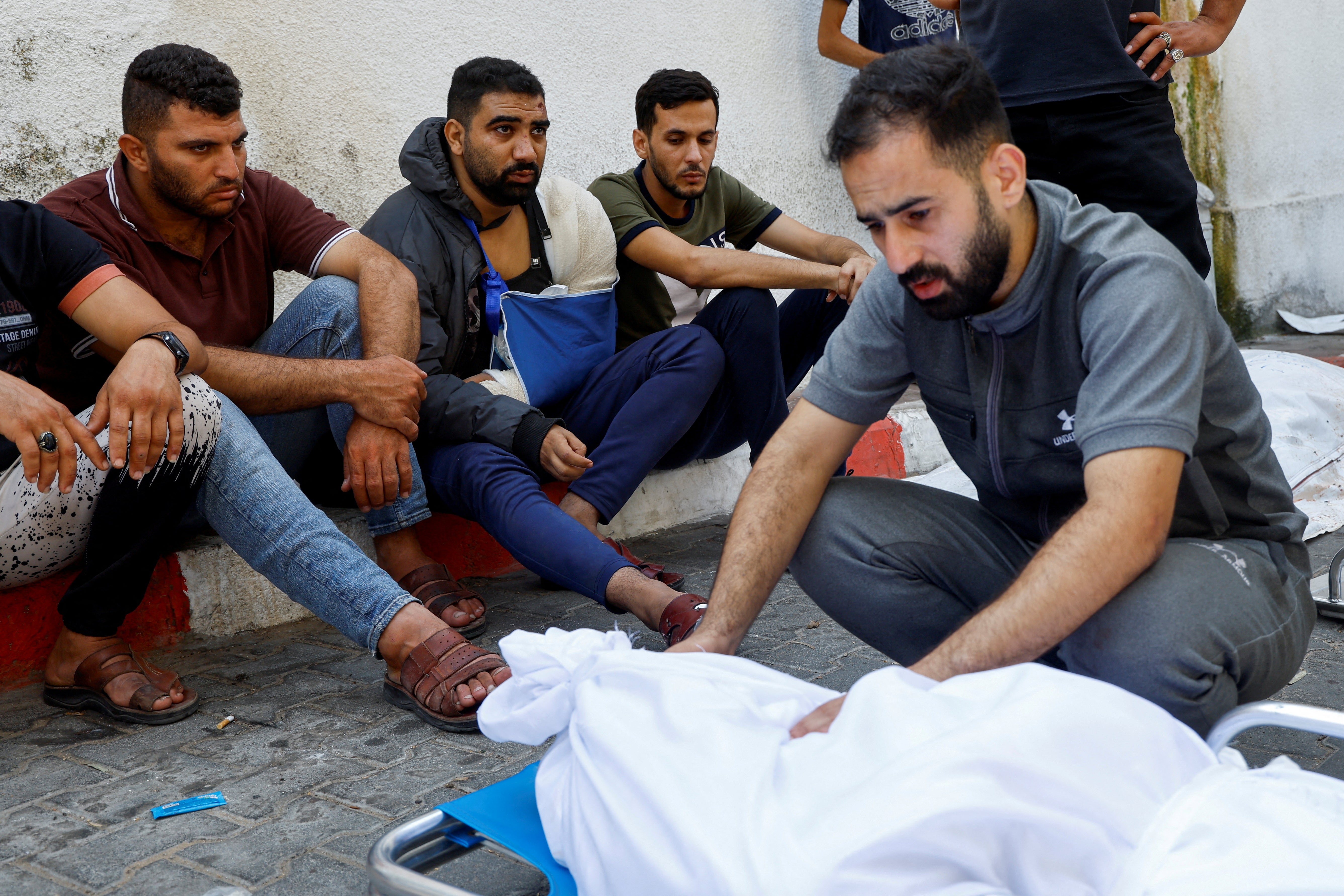Wounded Palestinian man Ala Al-Kafarneh (second left) sits by the bodies of his pregnant wife and extended family