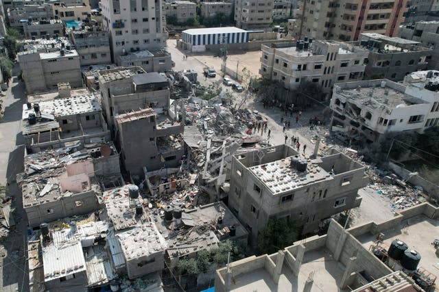 Palestinians stand by the building destroyed in an Israeli airstrike in Nuseirat camp in the central Gaza Strip (Hatem Moussa/AP)