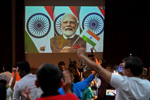 <p>People wave India’s national flag as India’s Prime Minister Narendra Modi (C screen) congratulates the Indian Space Research Organisation (ISRO) for the successful lunar landing of Chandrayaan-3 spacecraft on the south pole of the Moon during a live stream of the event at the Nehru Science Centre in Mumbai on August 23, 2023)</p>