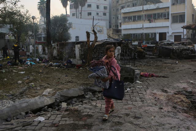 A Palestinian girl carries a blanket as she walks past the site of a deadly explosion at al Ahli hospital, in Gaza City (Abed Khaled/AP/PA)