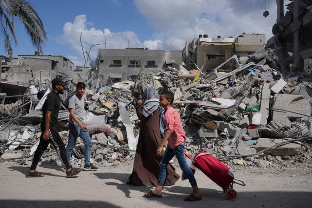 <p>Palestinians walk by buildings destroyed in Israeli airstrikes in Bureij refugee camp in Gaza on 18 October</p>