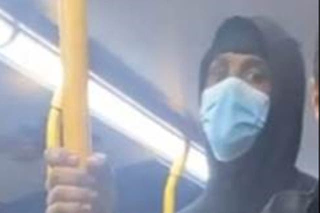 <p>A masked man looks directly into a camera as he rides a west London bus </p>