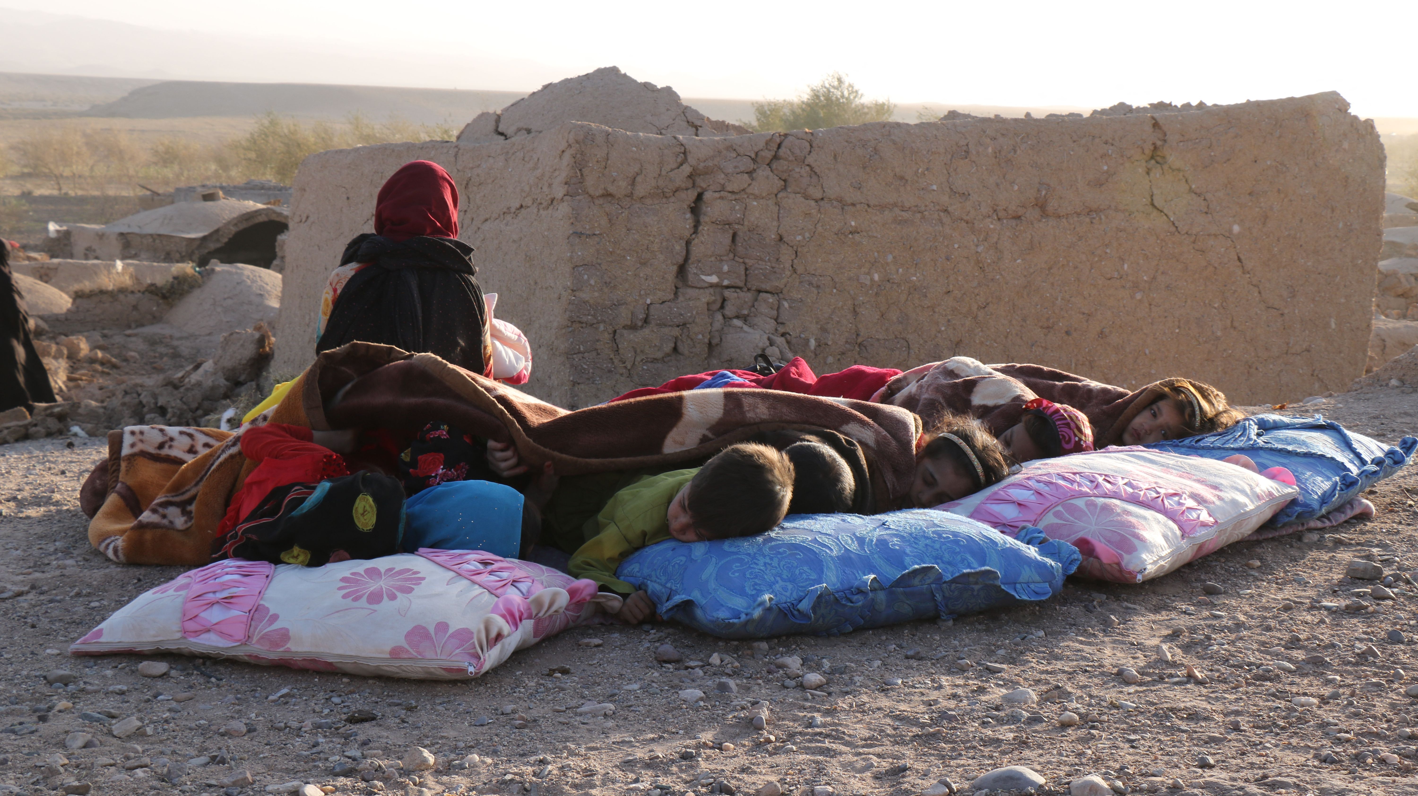 <p>Afghan children rest under a blanket beside damaged houses after earthquake in Sarbuland village of Zenda Jan district of Herat province</p>