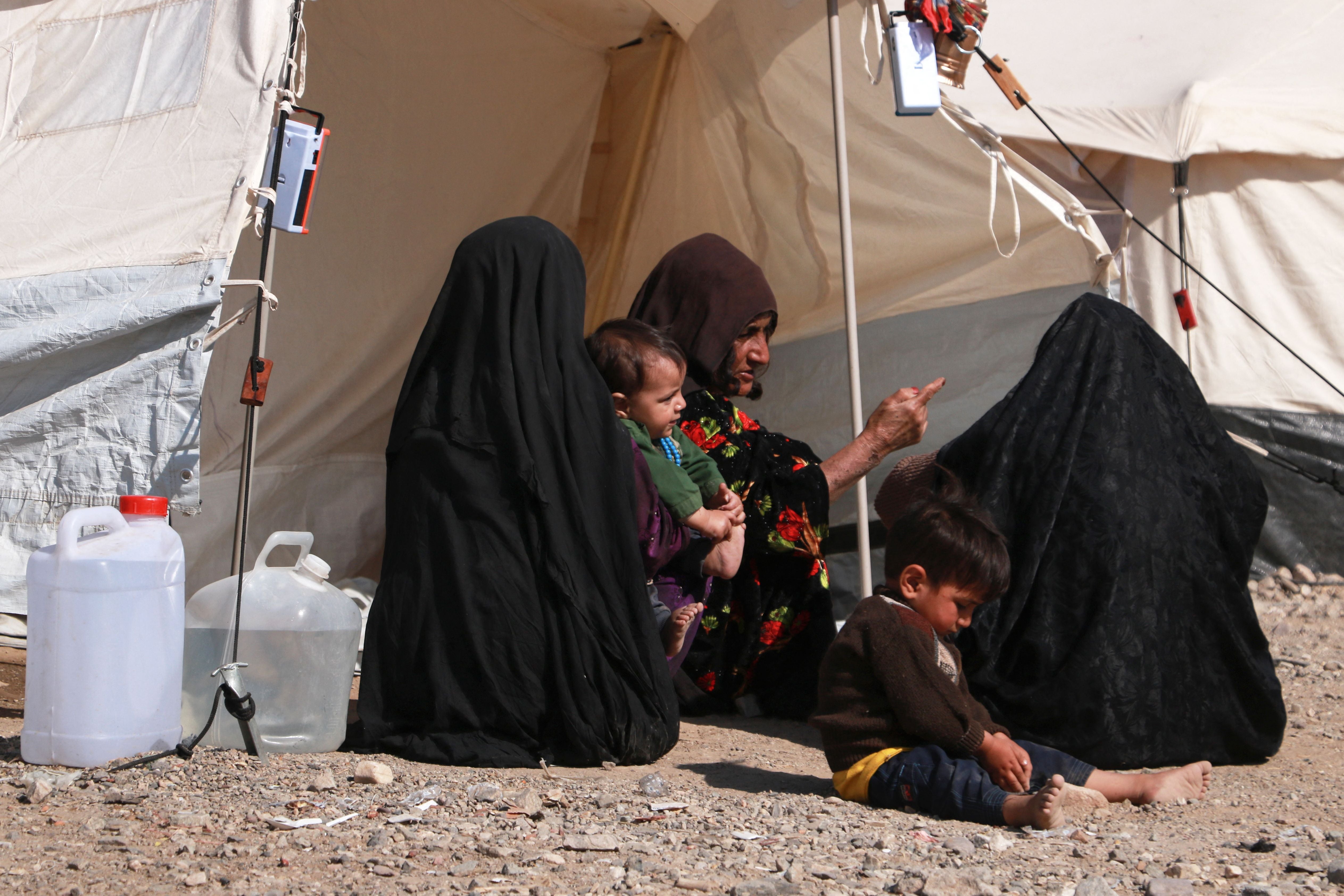 Afghan women and children sit outside their makeshift shelters at a camp set-up after earthquake on the outskirts of Herat