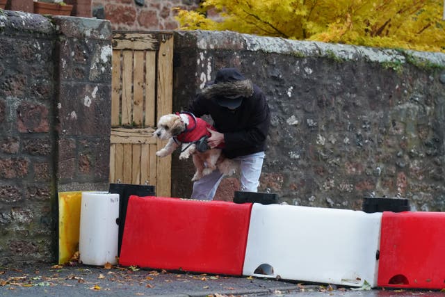 A man lifts his dog over a flood defence barrier erected on Church Street in the village of Edzell, Scotland (Andrew Milligan/PA)