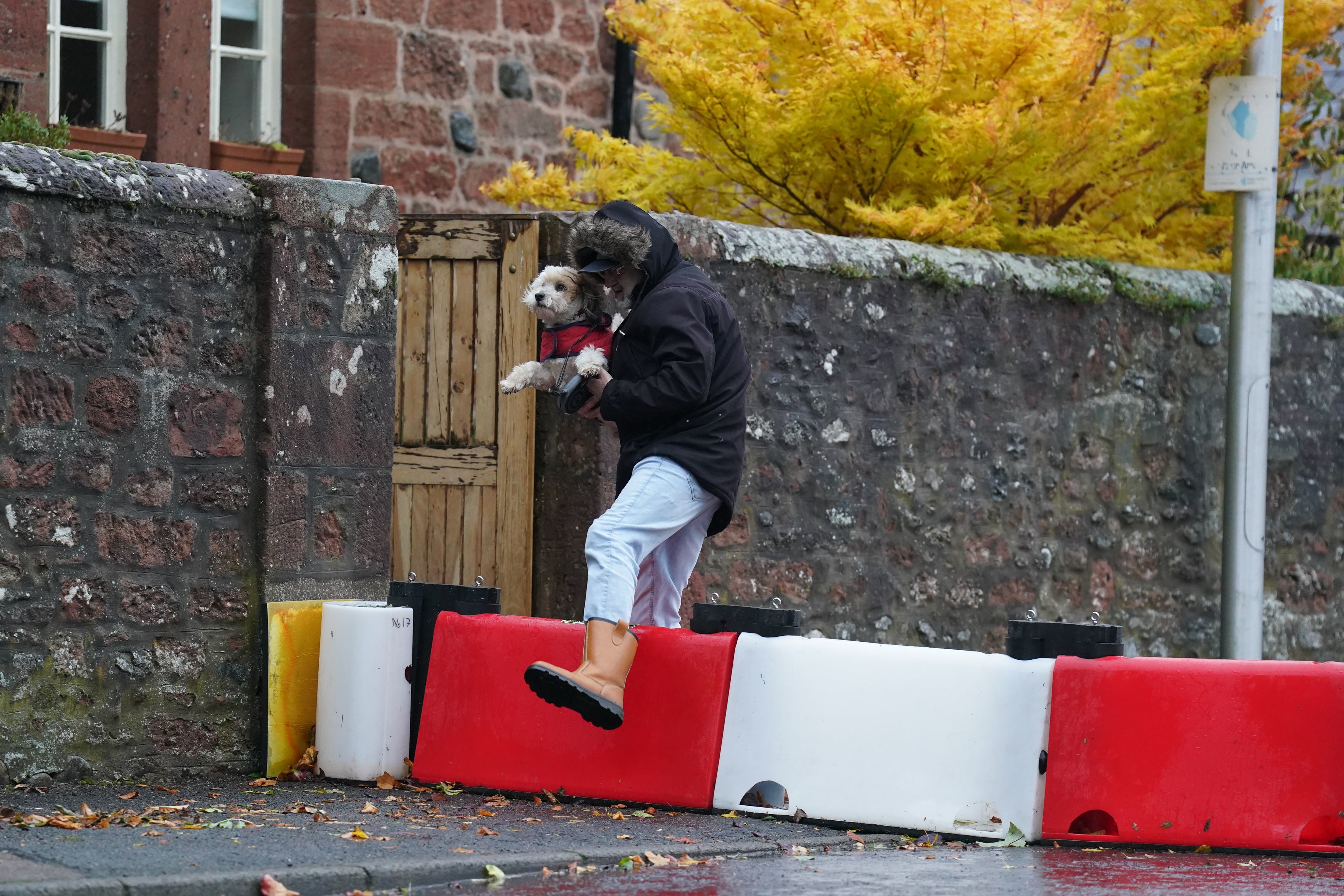 A man lifts his dog over a flood defence barrier erected on Church street in the village of Edzell