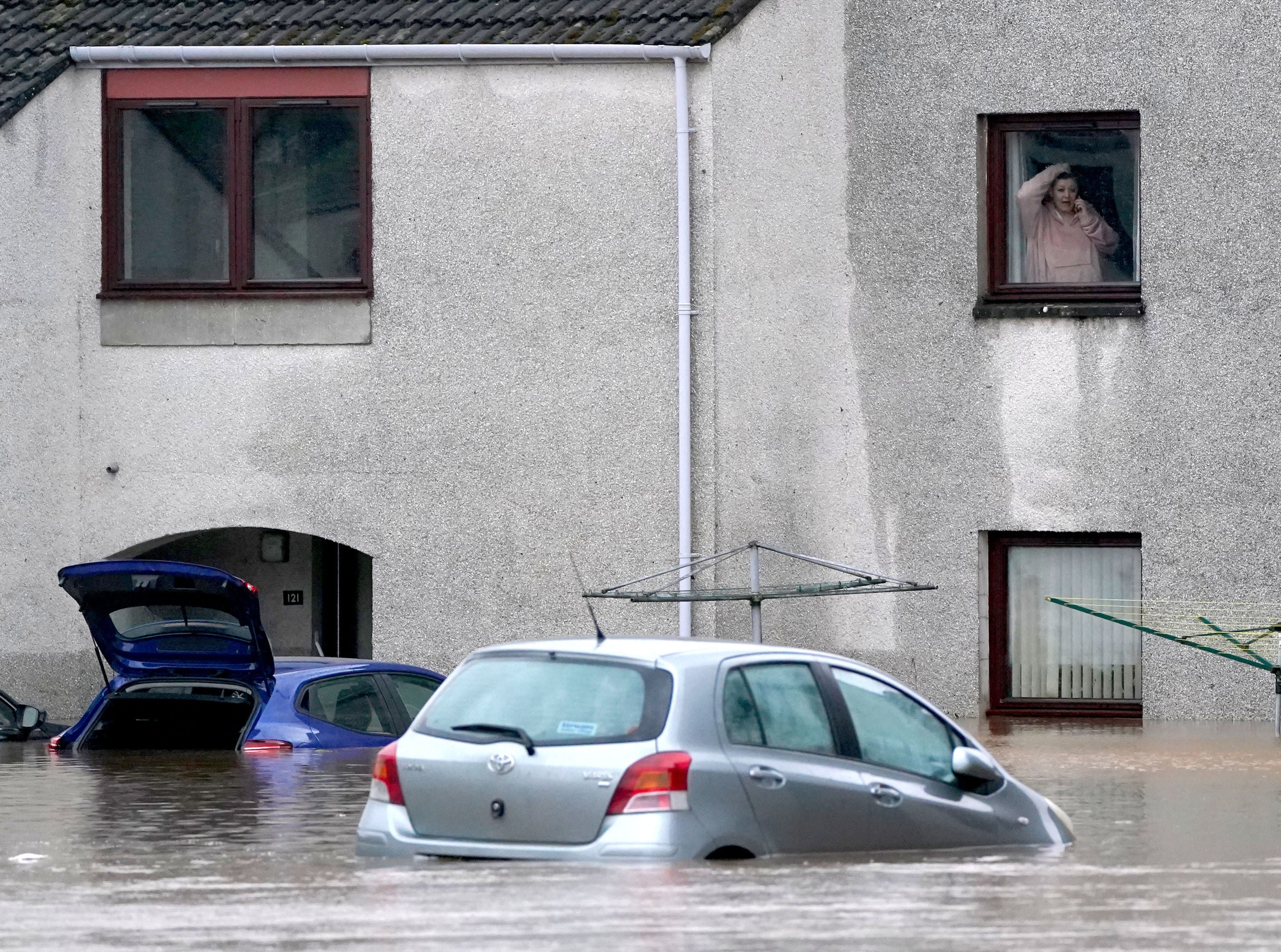A person looks from a window at a submerged car in flood water in Brechin, Scotland