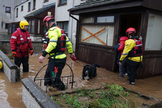 A member of the emergency services leads a dog from a house in Brechin as Storm Babet batters the country (Andrew Milligan/PA)