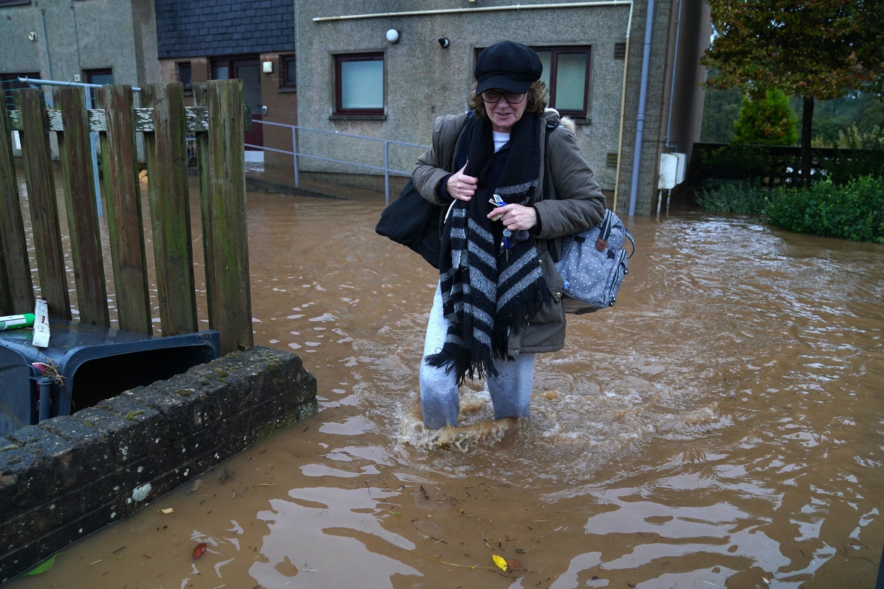 A woman wades through floodwater while clutching her belongings after Storm Babet battered Brechin, Scotland