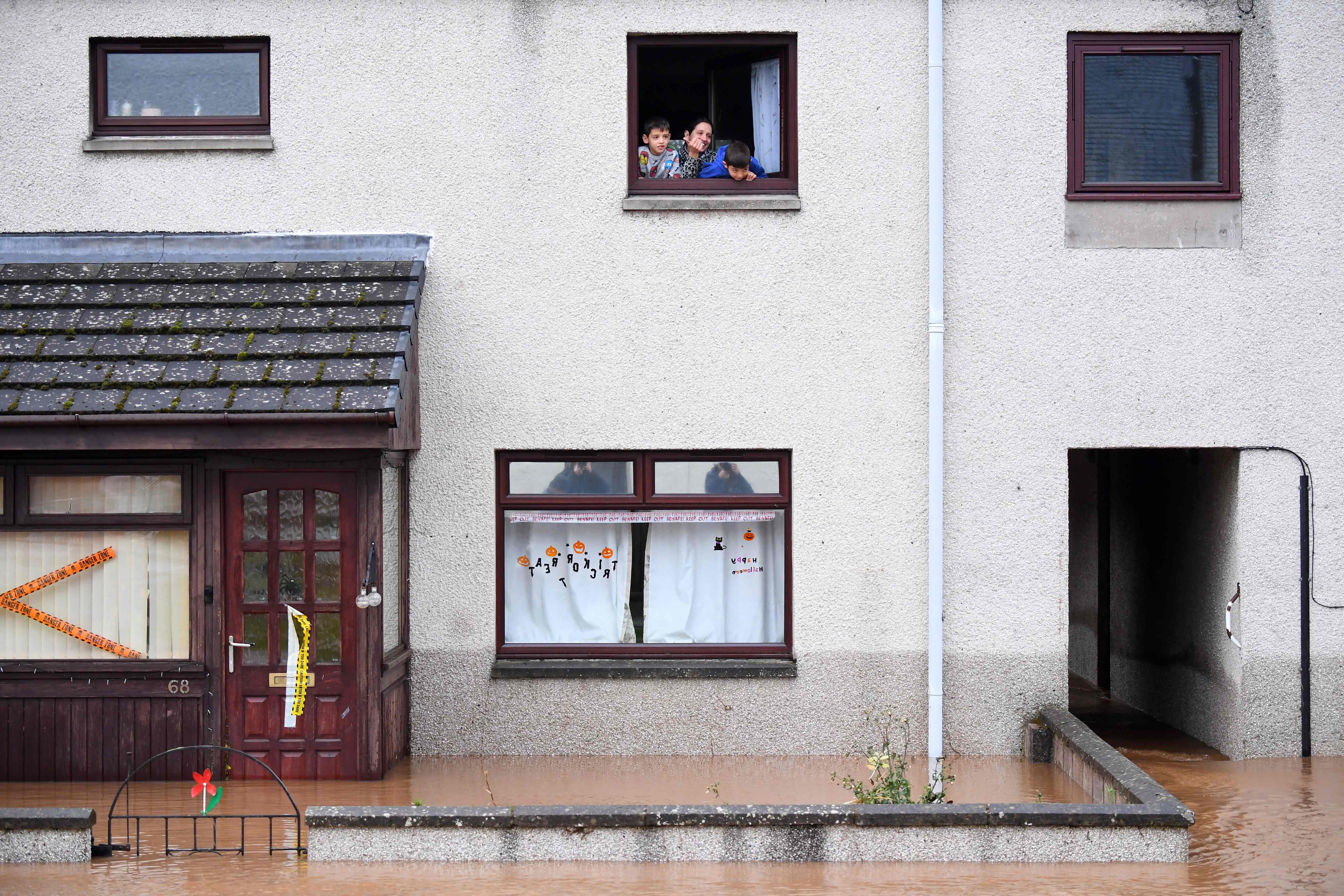 A family trapped in the upper floor of their home look out a window in a flooded stret in Brechin