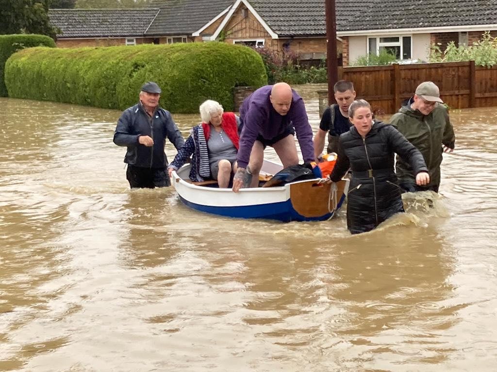 <p>Simon O'Brien (left) using his homemade boat, which he built for his grandchildren, to rescue elderly residents from their home in the village of Debenham, Suffolk</p>