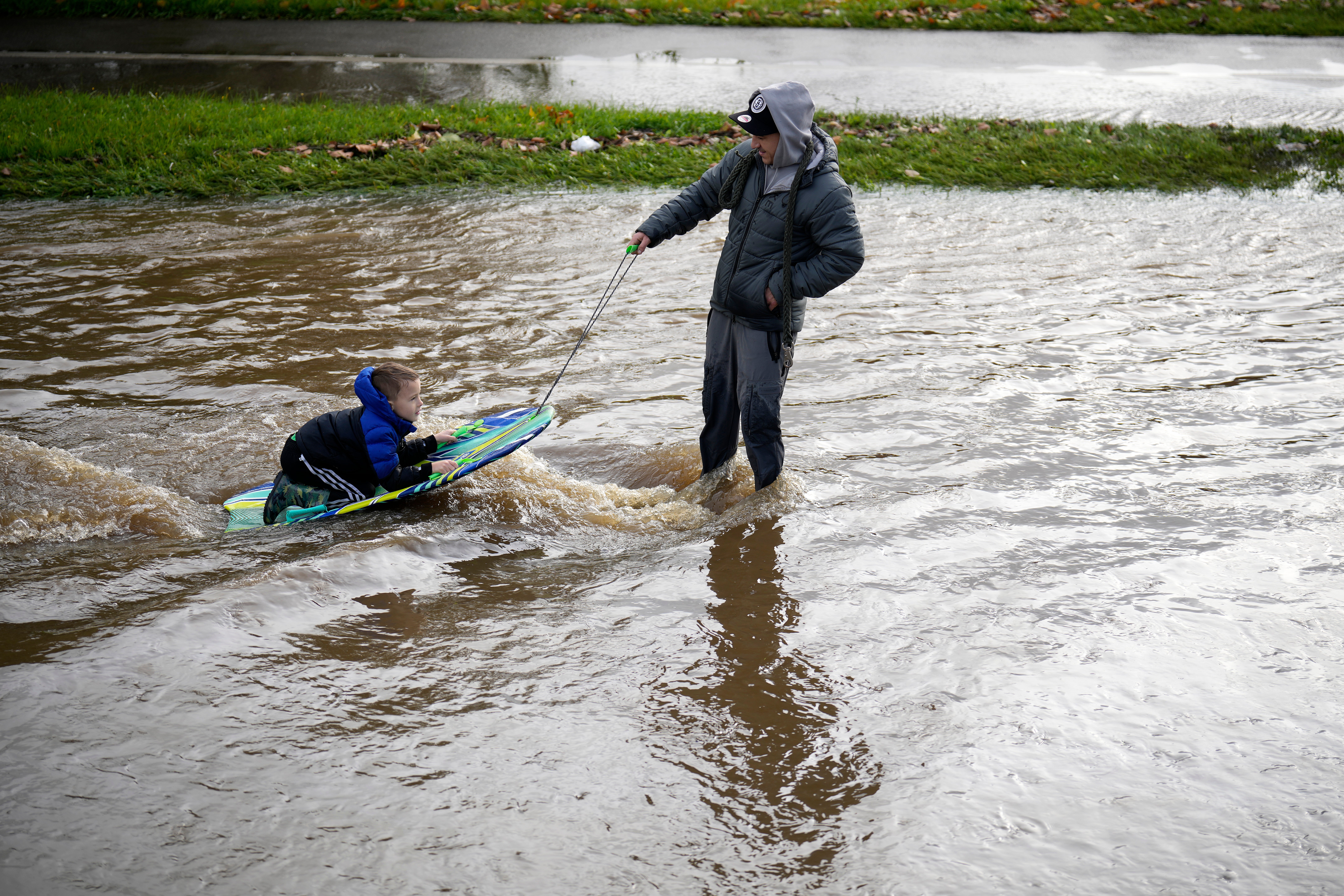 A man pulls a boy on a bodyboard through floodwater