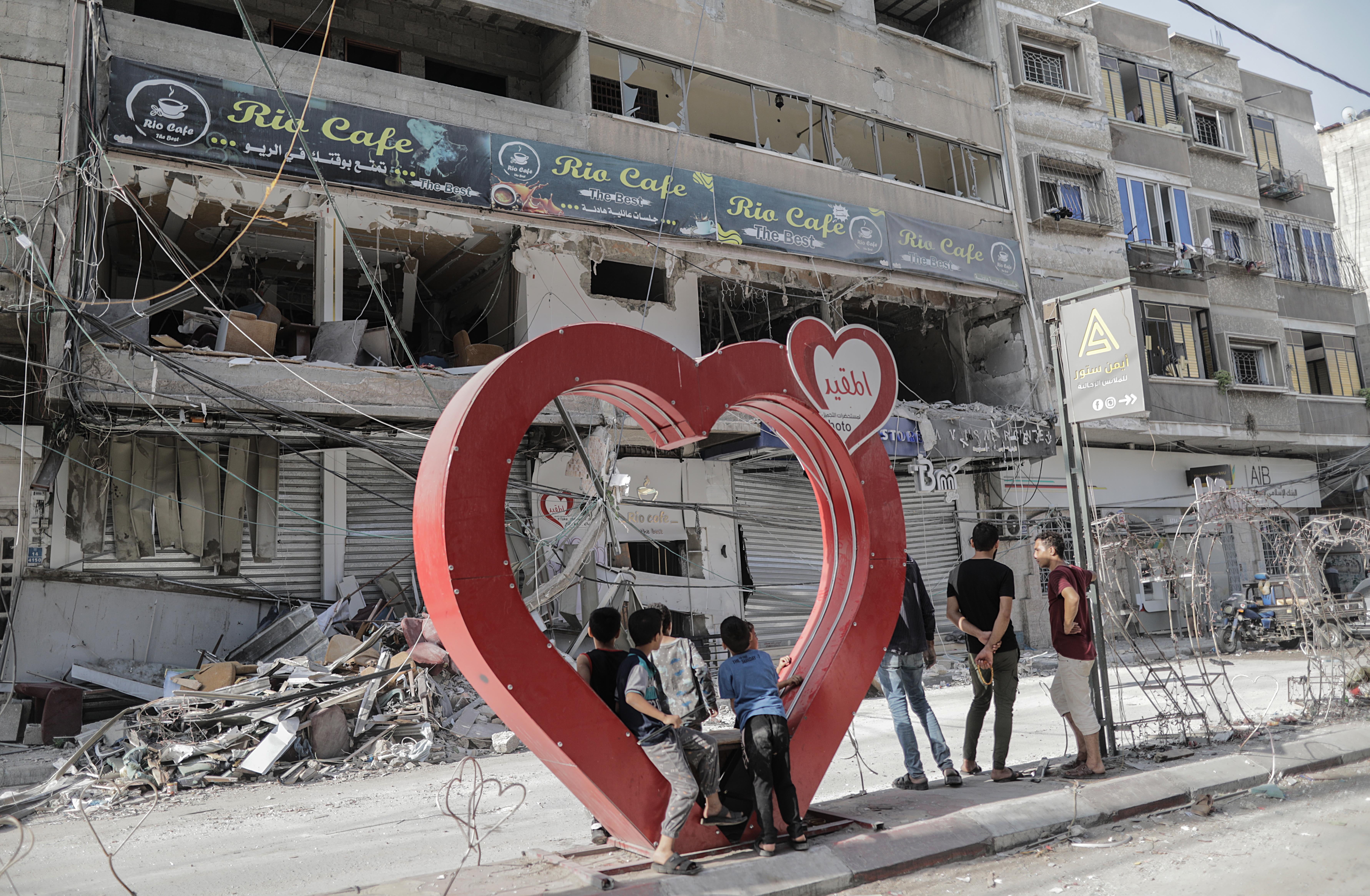 Palestinian youths stand on a heart-shaped installation next to the rubble of a building following an Israeli airstrike on Khan Younis refugee camp, southern Gaza Strip, on Sunday