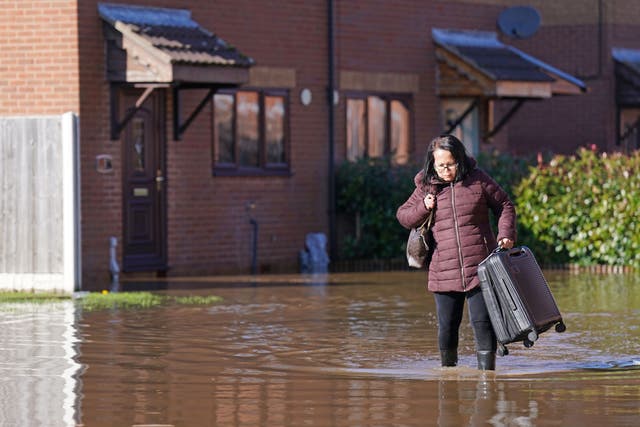 A resident with a suitcase walks through flood water in Retford in Nottinghamshire (Joe Giddens/PA)