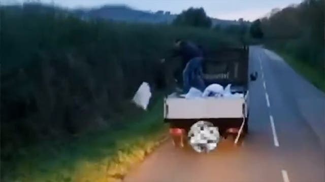 <p>Fly-tipper standing brazenly throws bags of rubbish into countryside lane.</p>