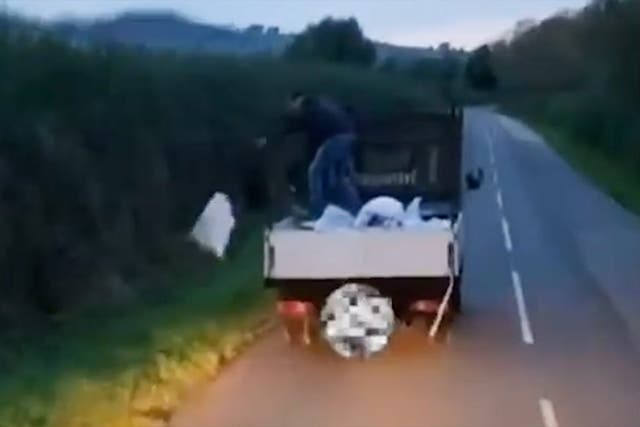 <p>Fly-tipper standing brazenly throws bags of rubbish into countryside lane.</p>