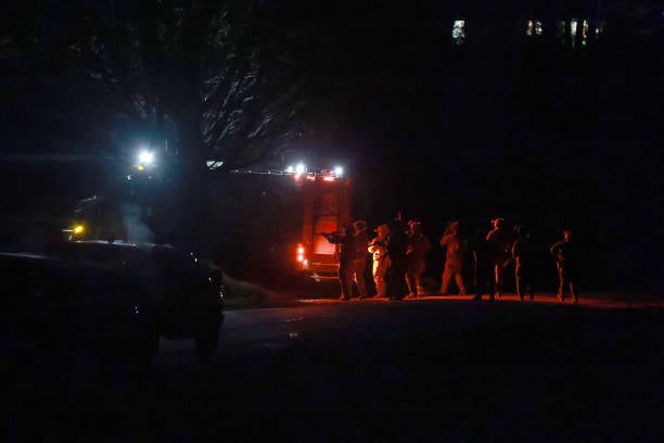 <p>Law Enforcement officials gather near a home as they prepare to search it for the suspect in connection with two mass shootings on 26 October 2023 </p>