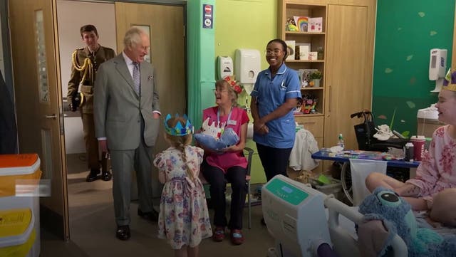 <p>King Charles presented with paper crown by young girl at new hospice opening.</p>