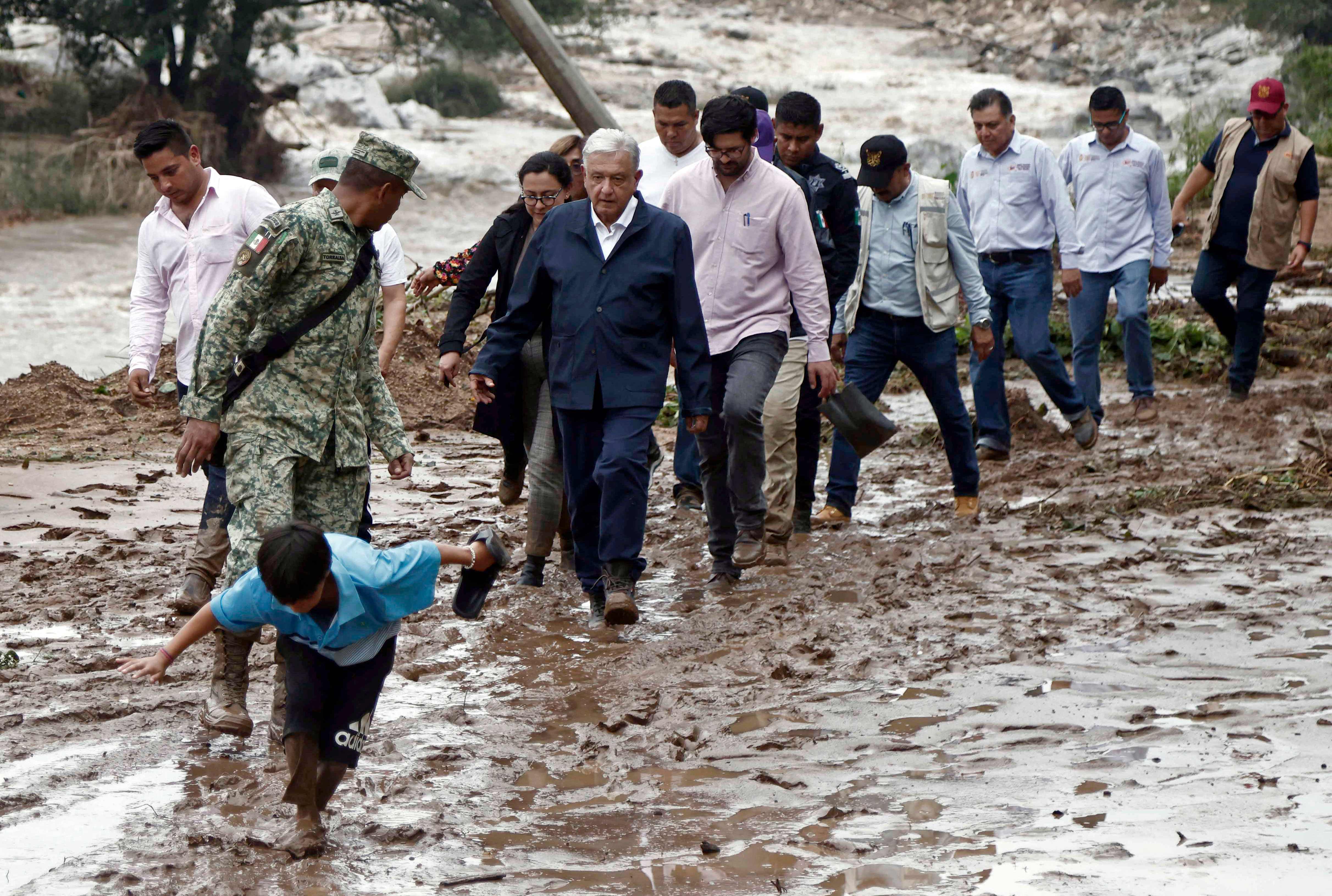 Lopez Obrador and members of his cabinet walk through mud as they visit the Kilometro 42 community, near Acapulco