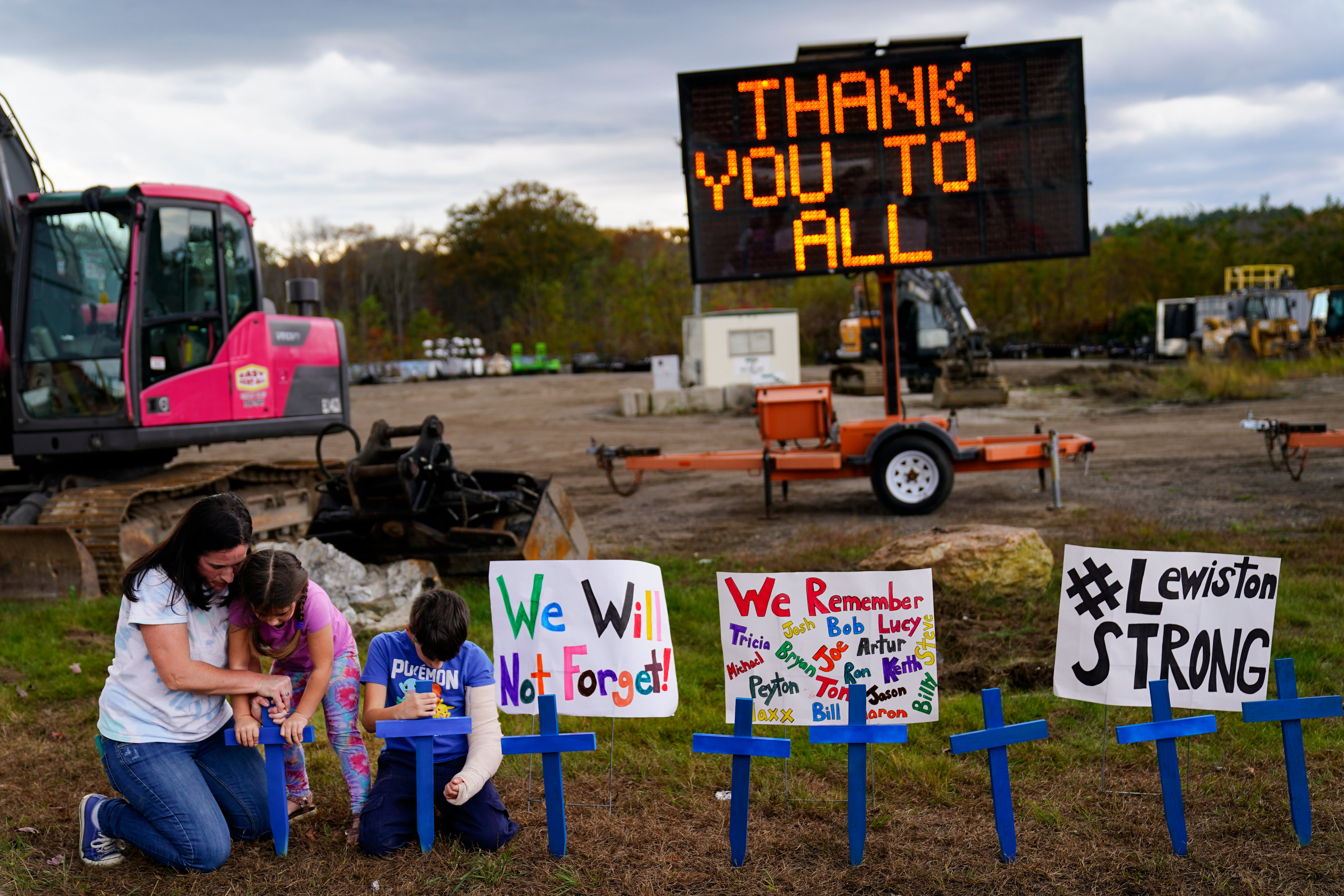 <p>A family sit in front of signs honouring the lives lost in Lewiston’s mass shooting </p>