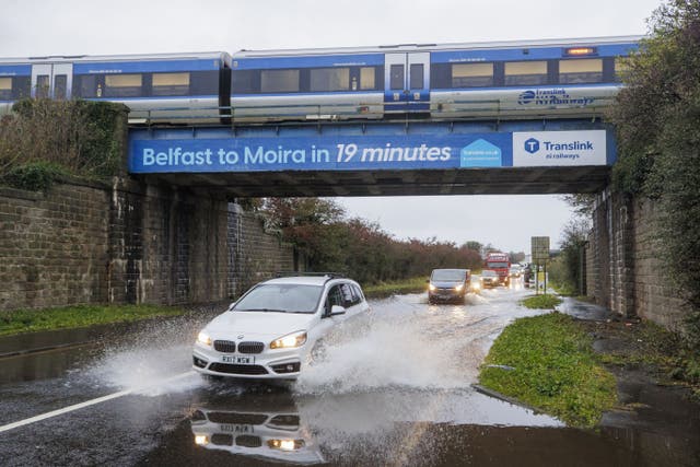 <p>A car drives through a flooded area under a railway bridge as a train passes overhead, on the A26 outside the village of Moira in Northern Ireland. Picture date: Monday 30 October 2023</p>