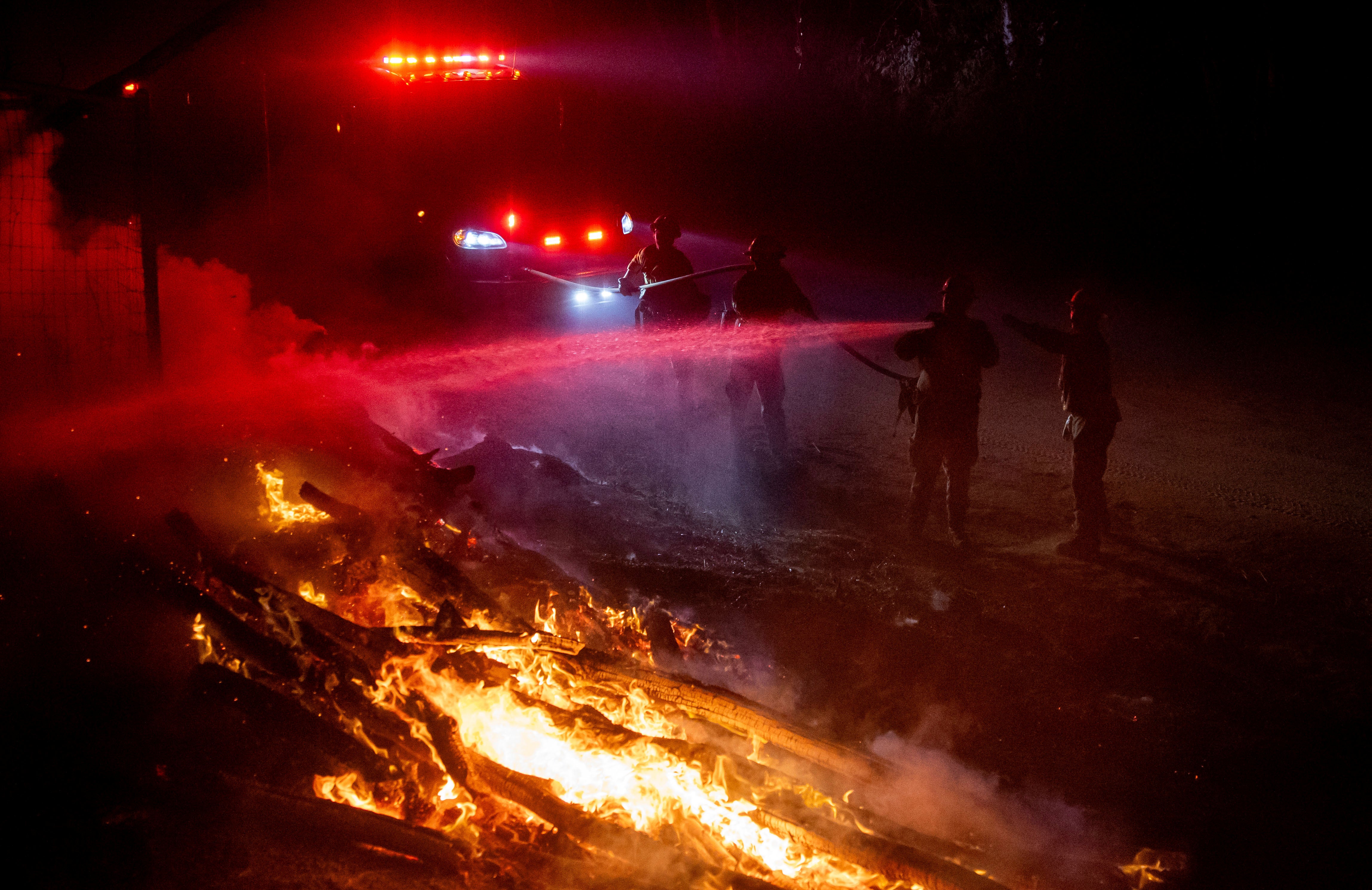 Firefighters douse flames while battling the Highland Fire in Aguanga on Monday