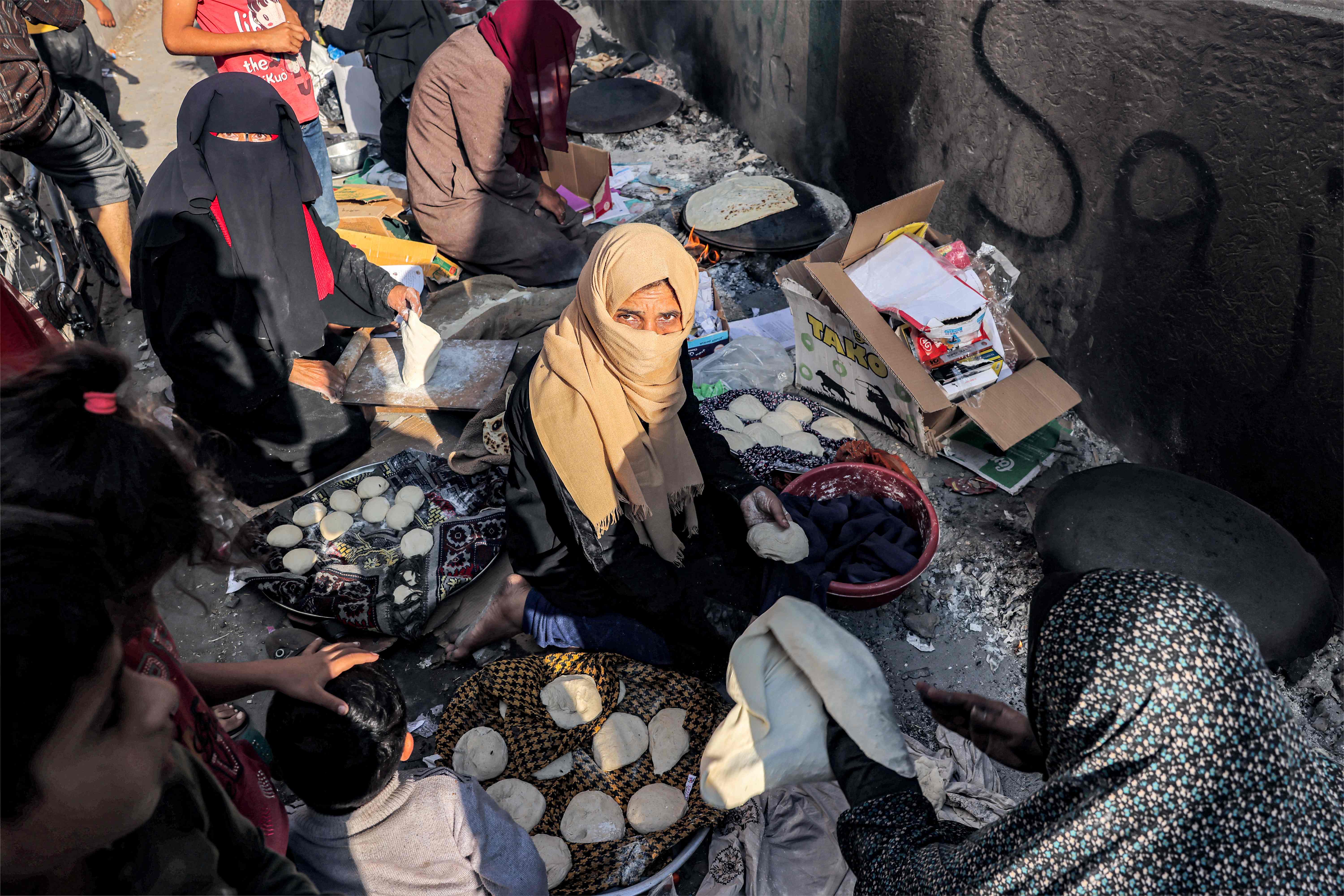 Women sit baking traditional flatbread along an alley in Rafah in southern Gaza Strip on 1 November 2023 amid ongoing battles between Israel and the Palestinian Hamas movement