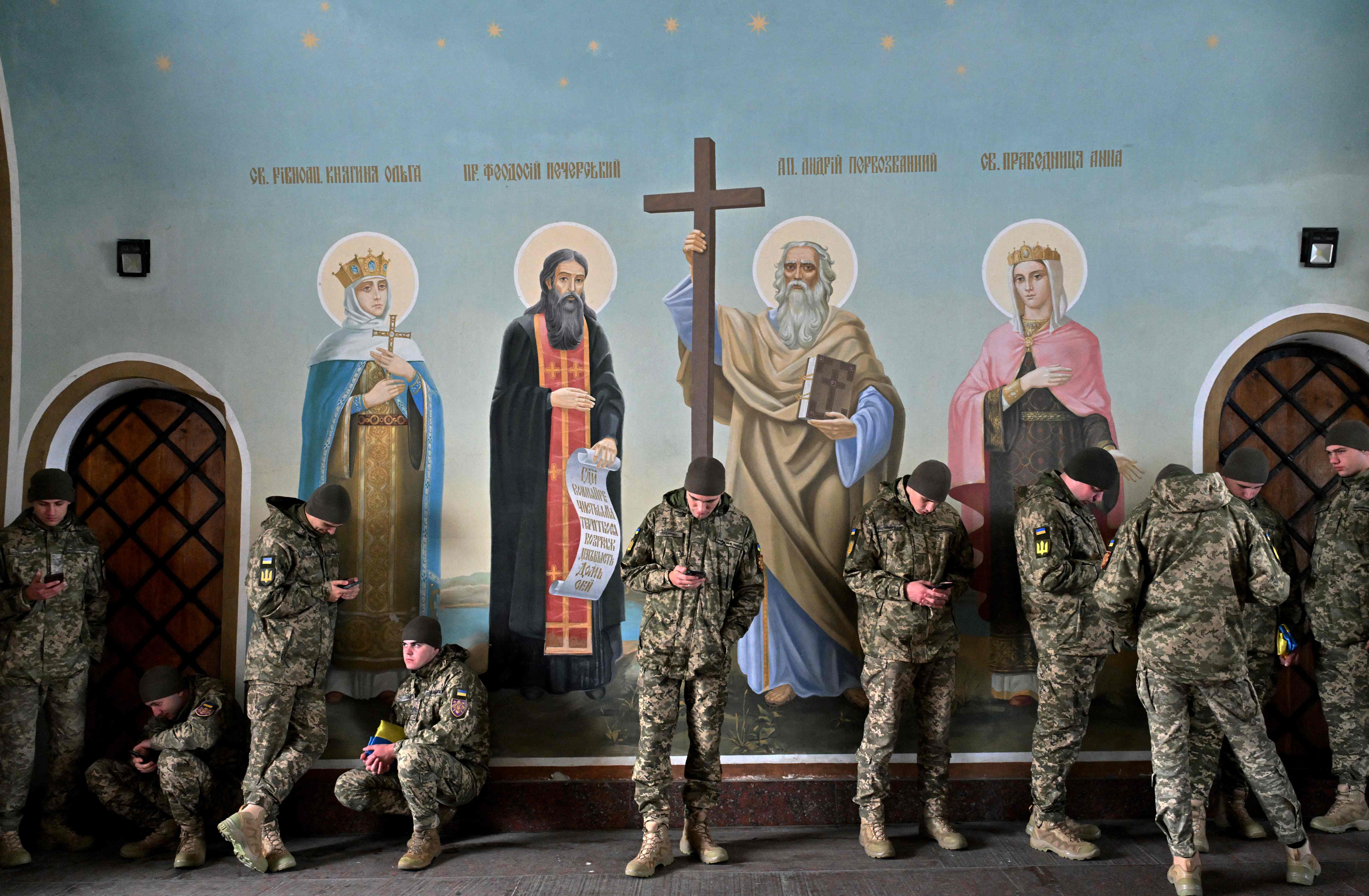 <p>Ukrainian servicemen look at their phones as they shelter from the rain in St Michael’s Cathedral in Kyiv </p>