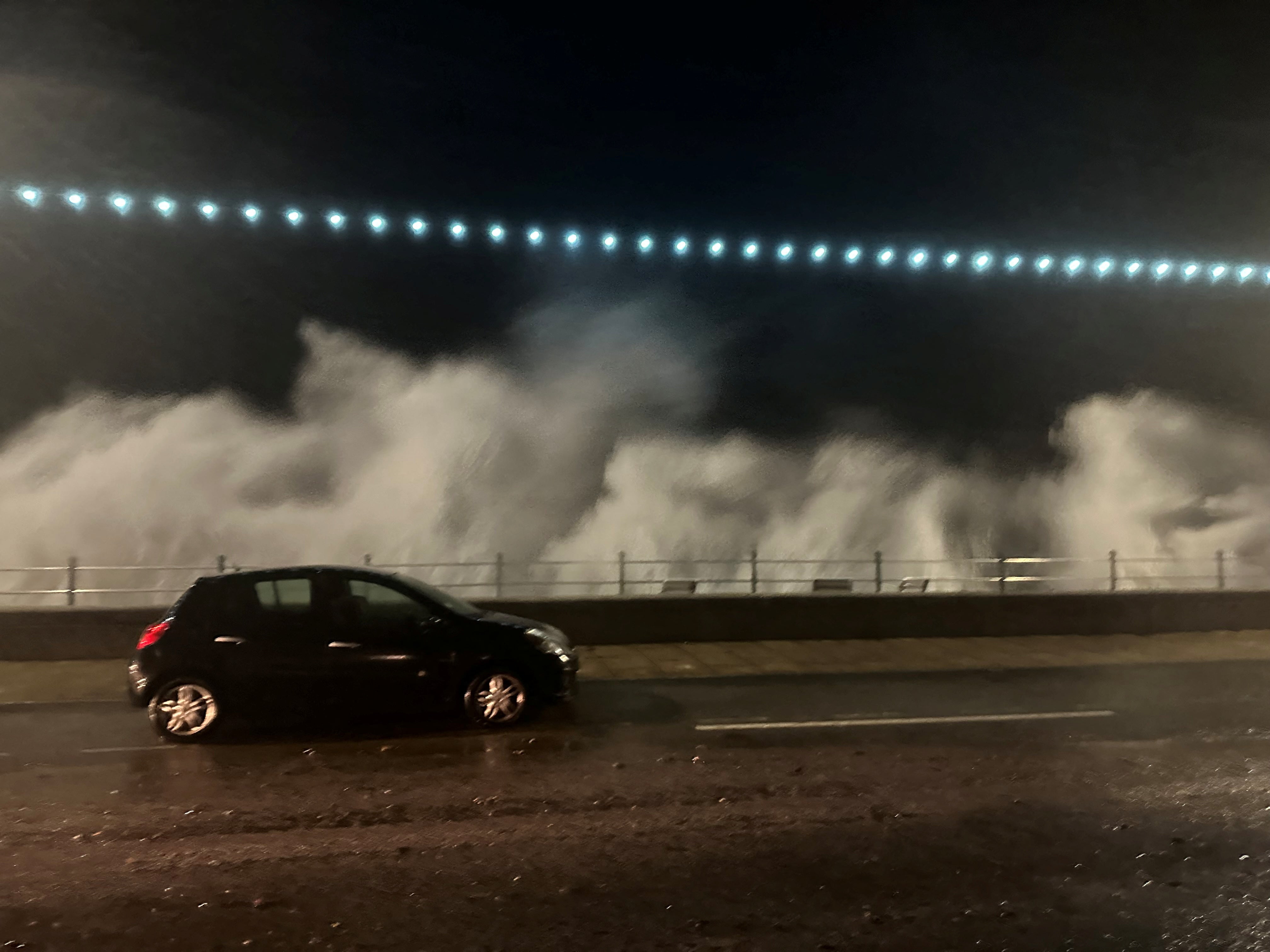 A vehicle passes by as the breeze of high waves caused by storm Ciaran is seen in the background, in Penzance, Cornwall