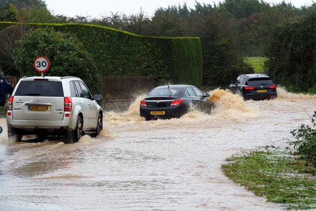 Vehicles are driven along a flooded road in Yapton, West Sussex (Joe Sene/PA)